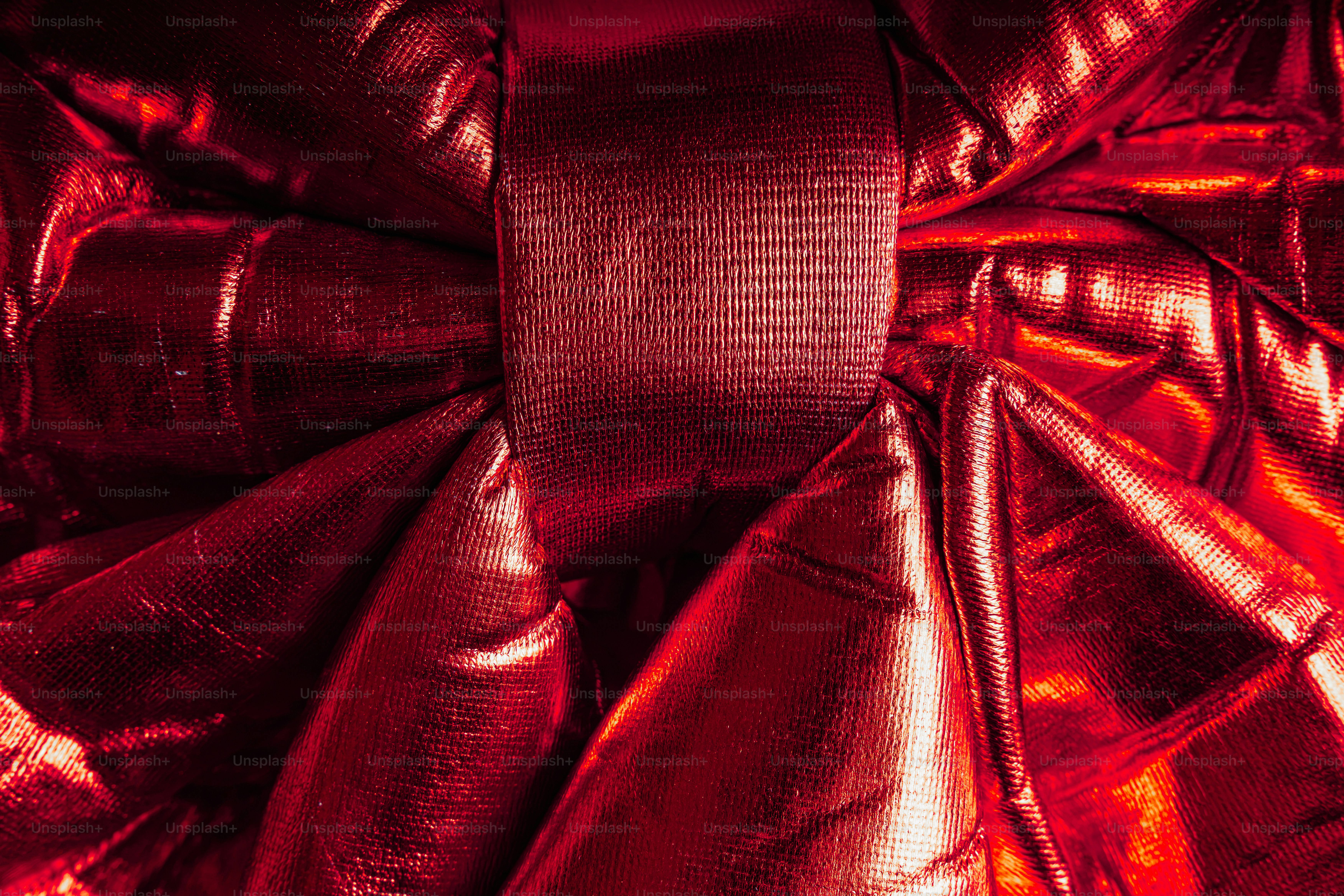 A close-up of a shiny red fabric bow with deep folds and creases