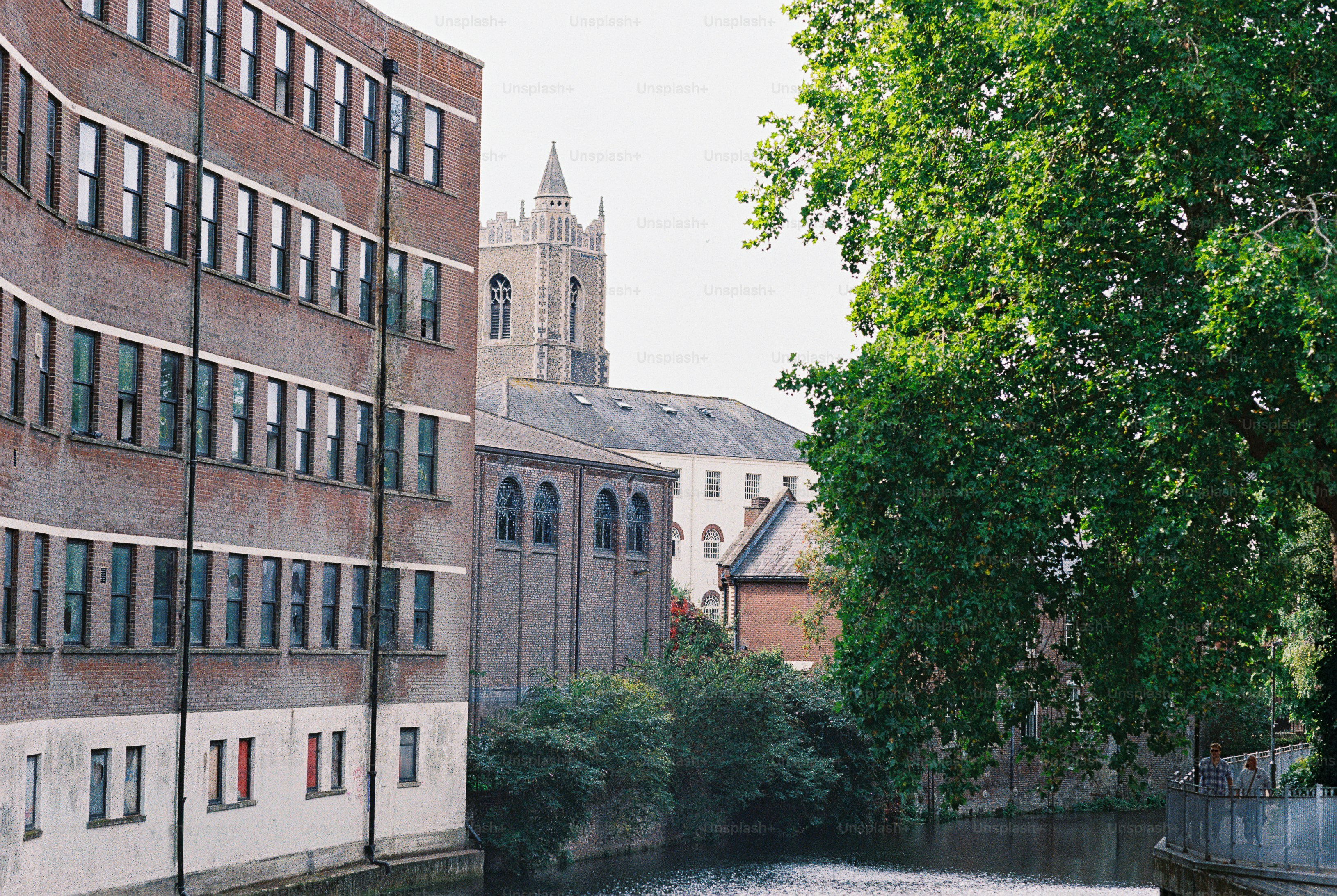 A brick building beside a canal with a church tower in the background