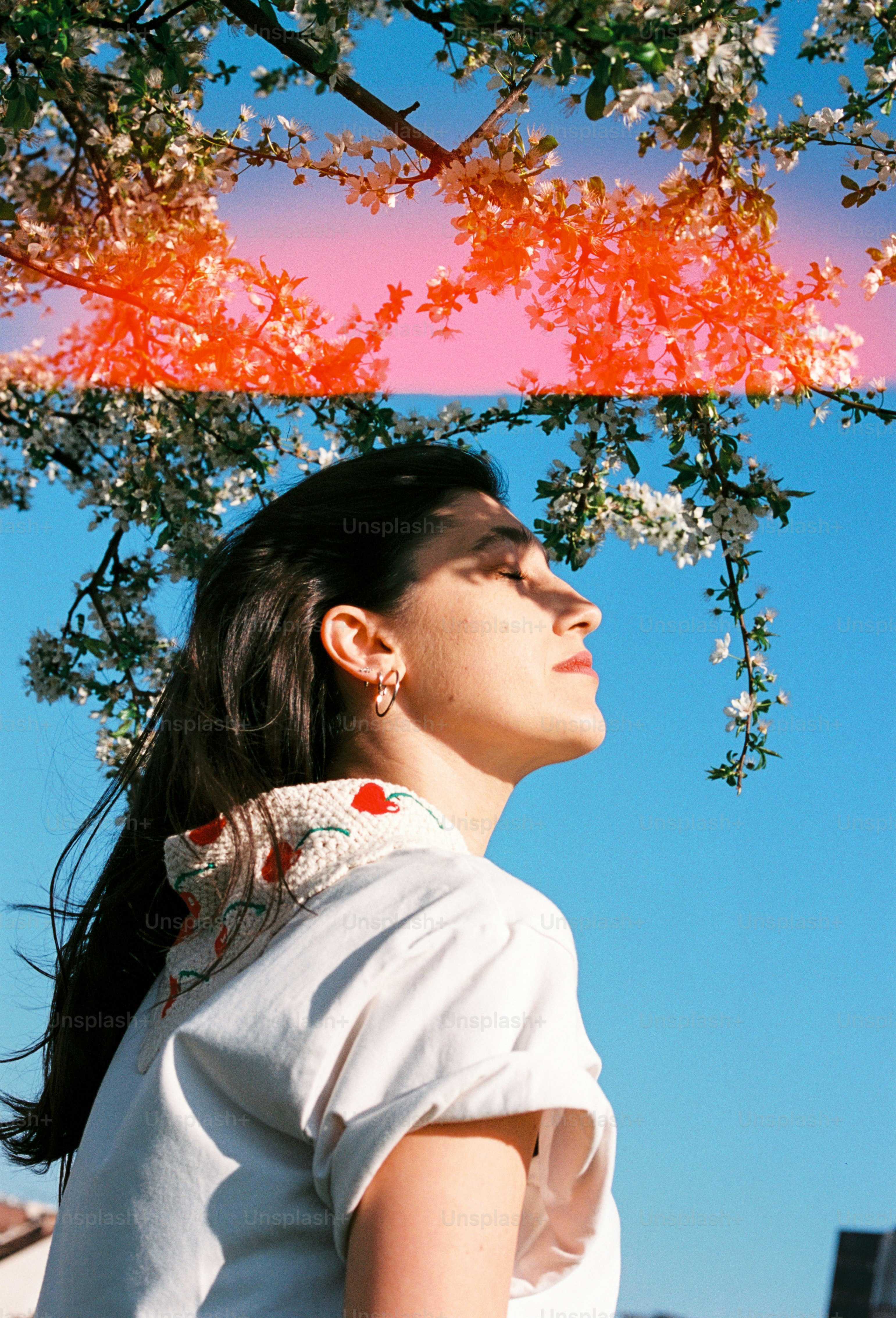 A woman with eyes closed beneath a flowering tree against a blue sky