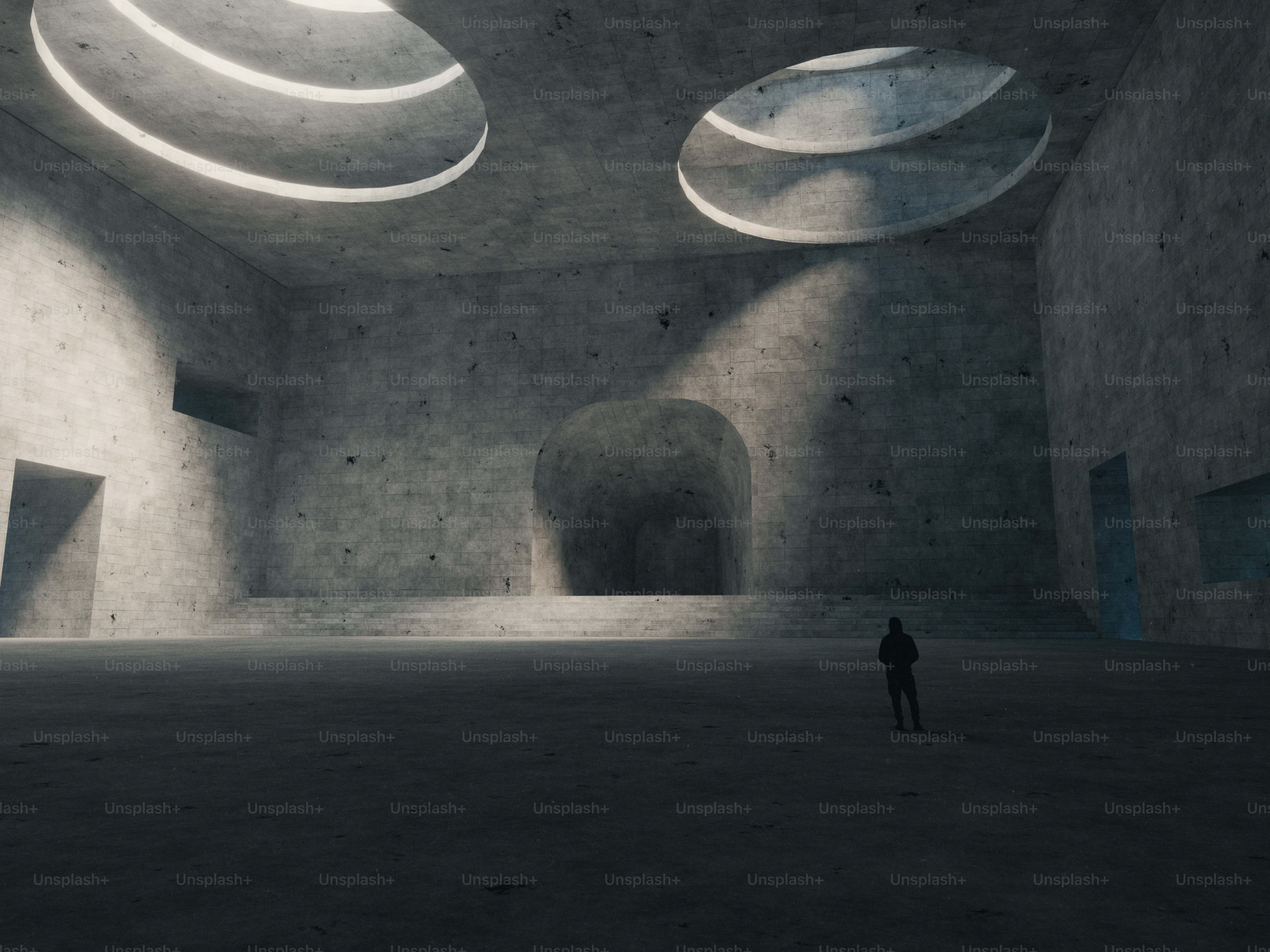 Una persona con una sudadera oscura de pie en un enorme salón de hormigón con tragaluces circulares