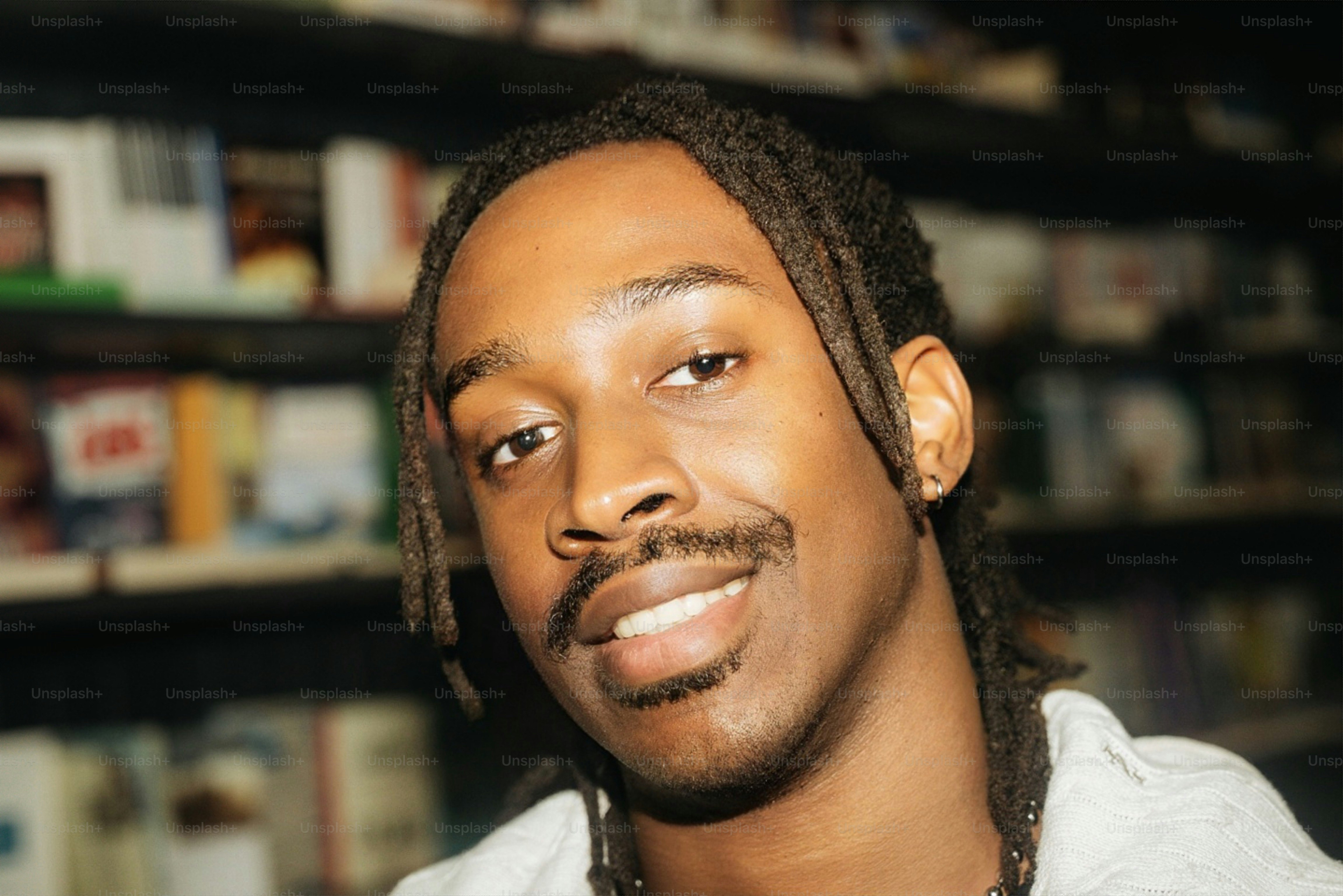 A smiling man with dreadlocks and a small hoop earring in a library