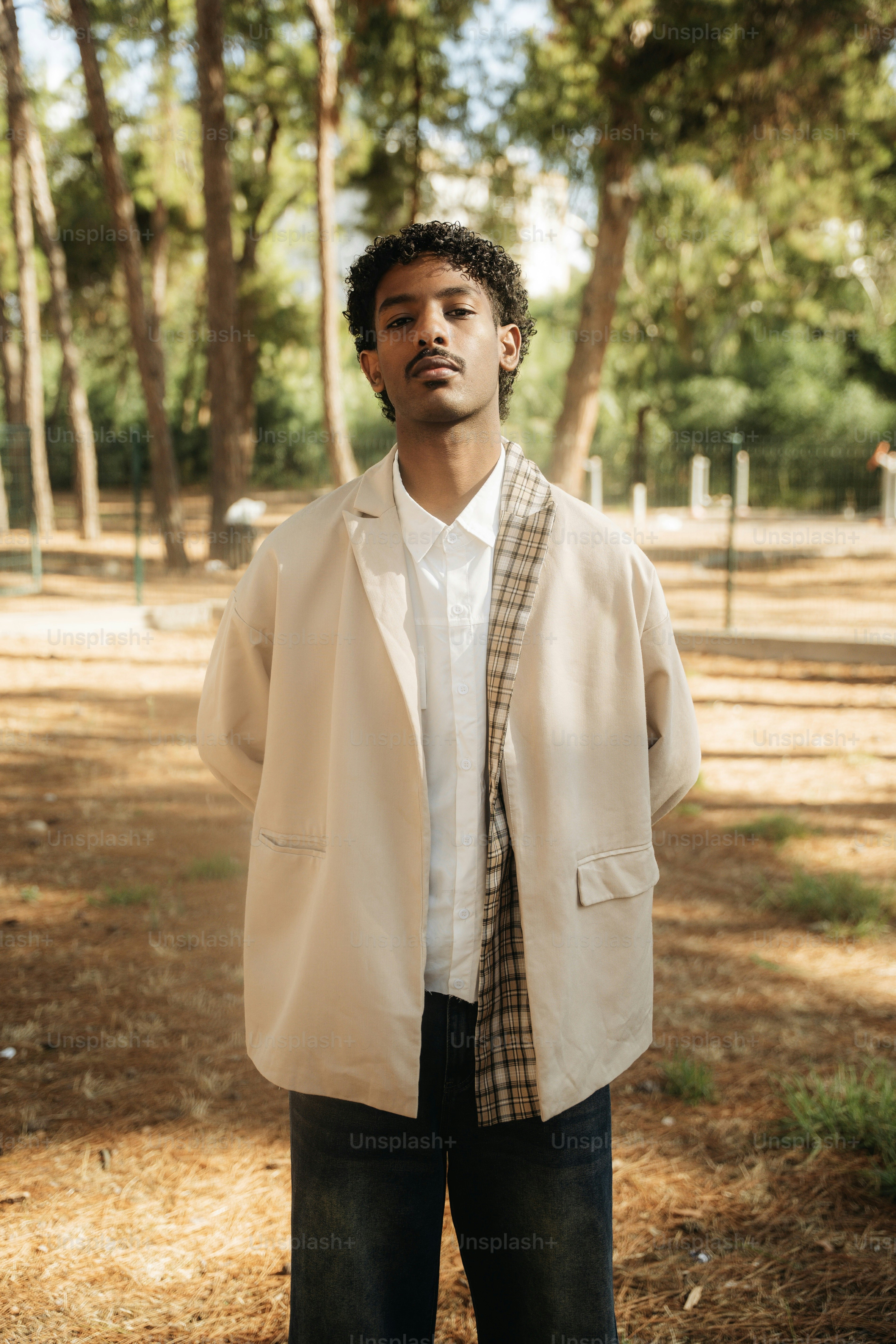 A young adult man in a beige blazer and white shirt in a sunlit pine forest