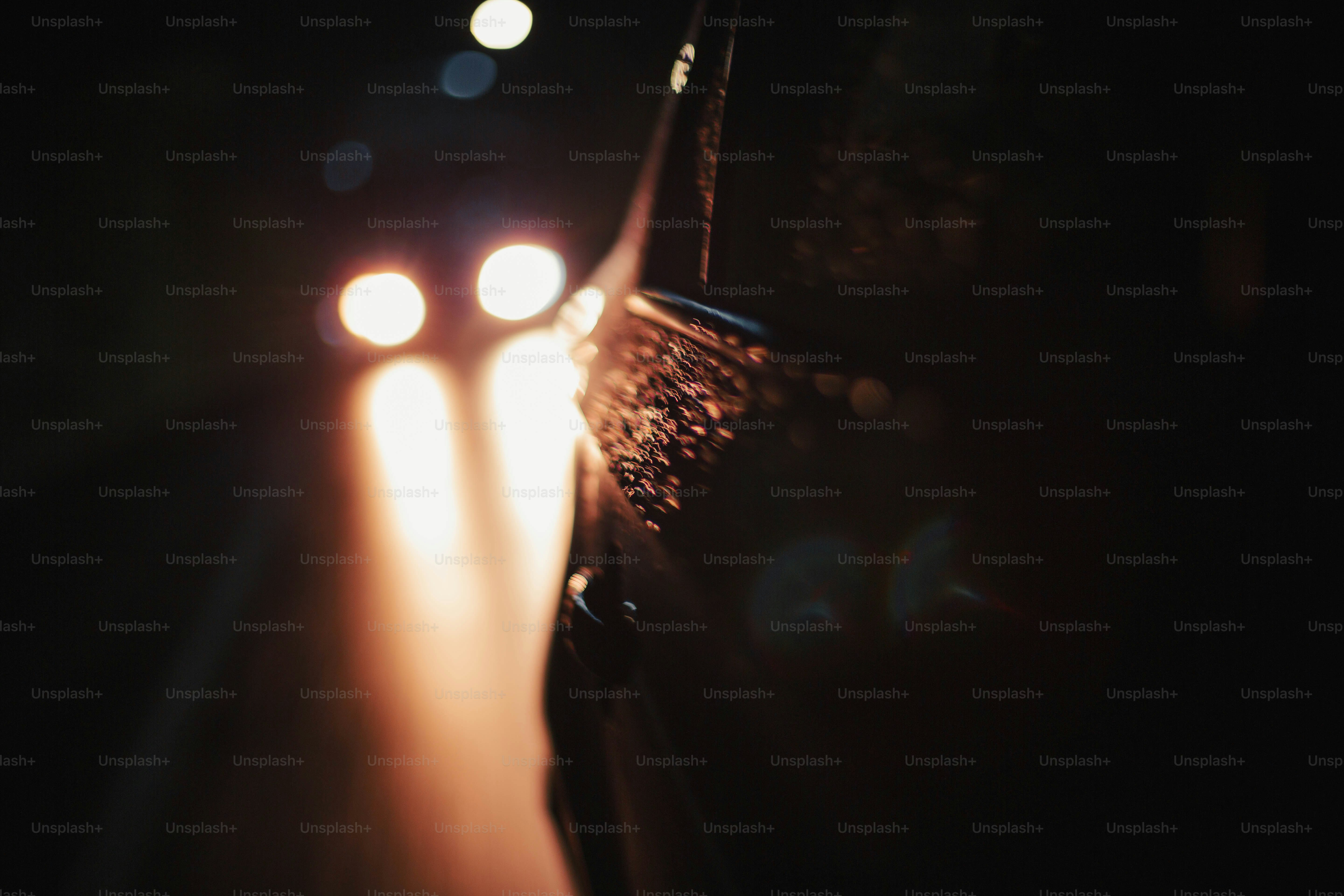 A dark car body with raindrops reflecting bright blurred headlights on a road at night