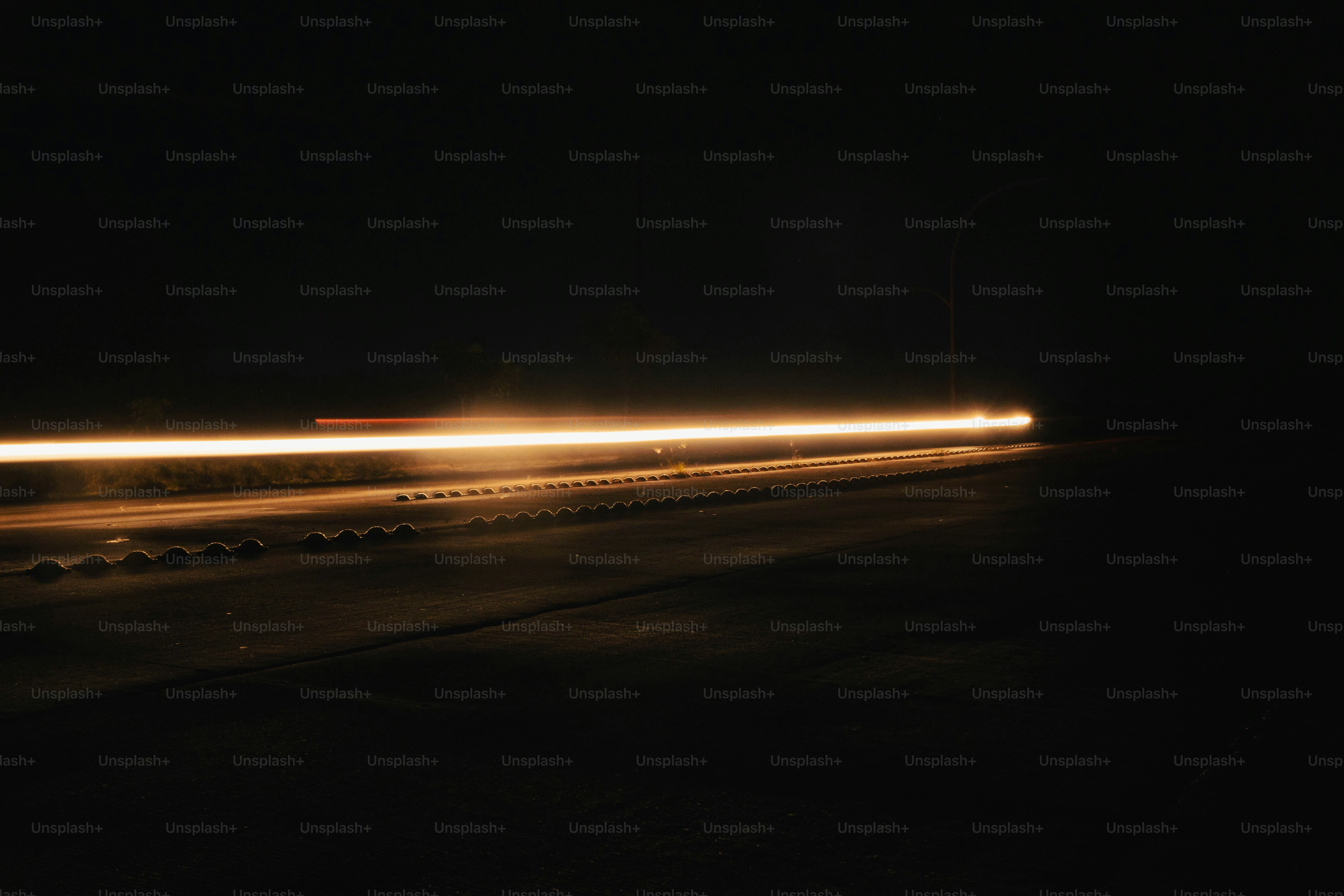A long exposure of a bright light trail from a vehicle on a dark road