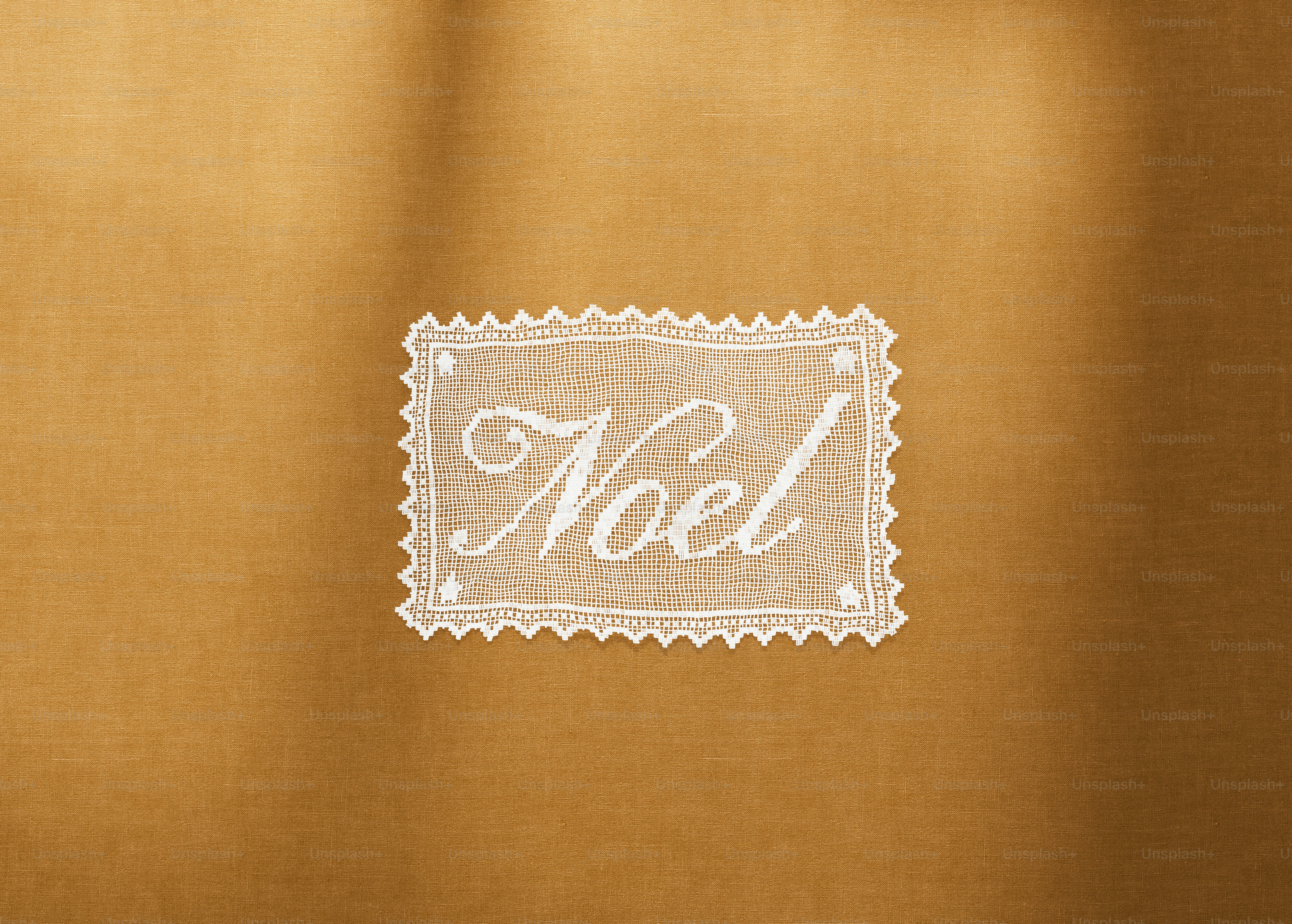 A white lace doily with the word Noel embroidered on a gold background