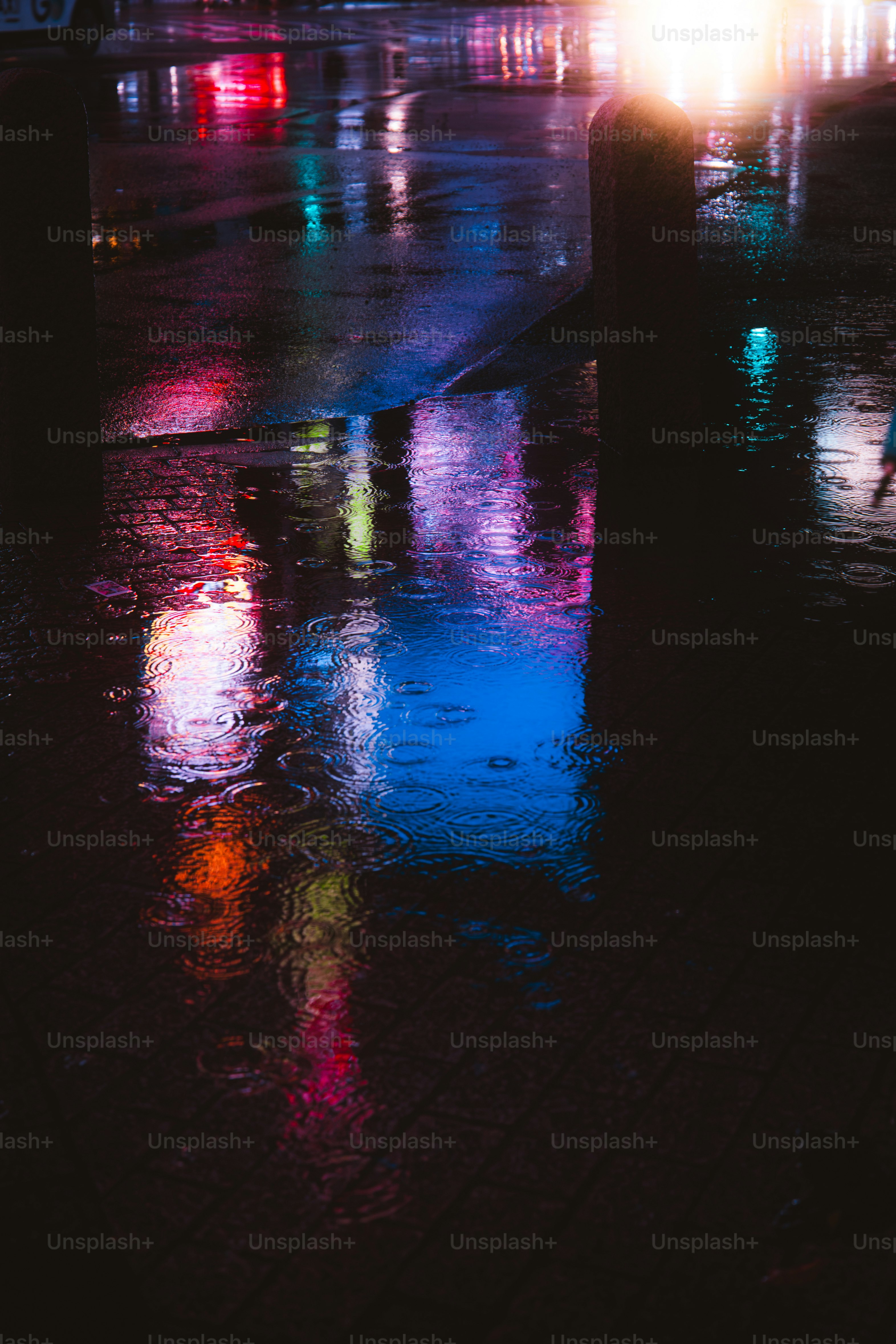 Neon light reflections in a rain puddle on a dark city street at night