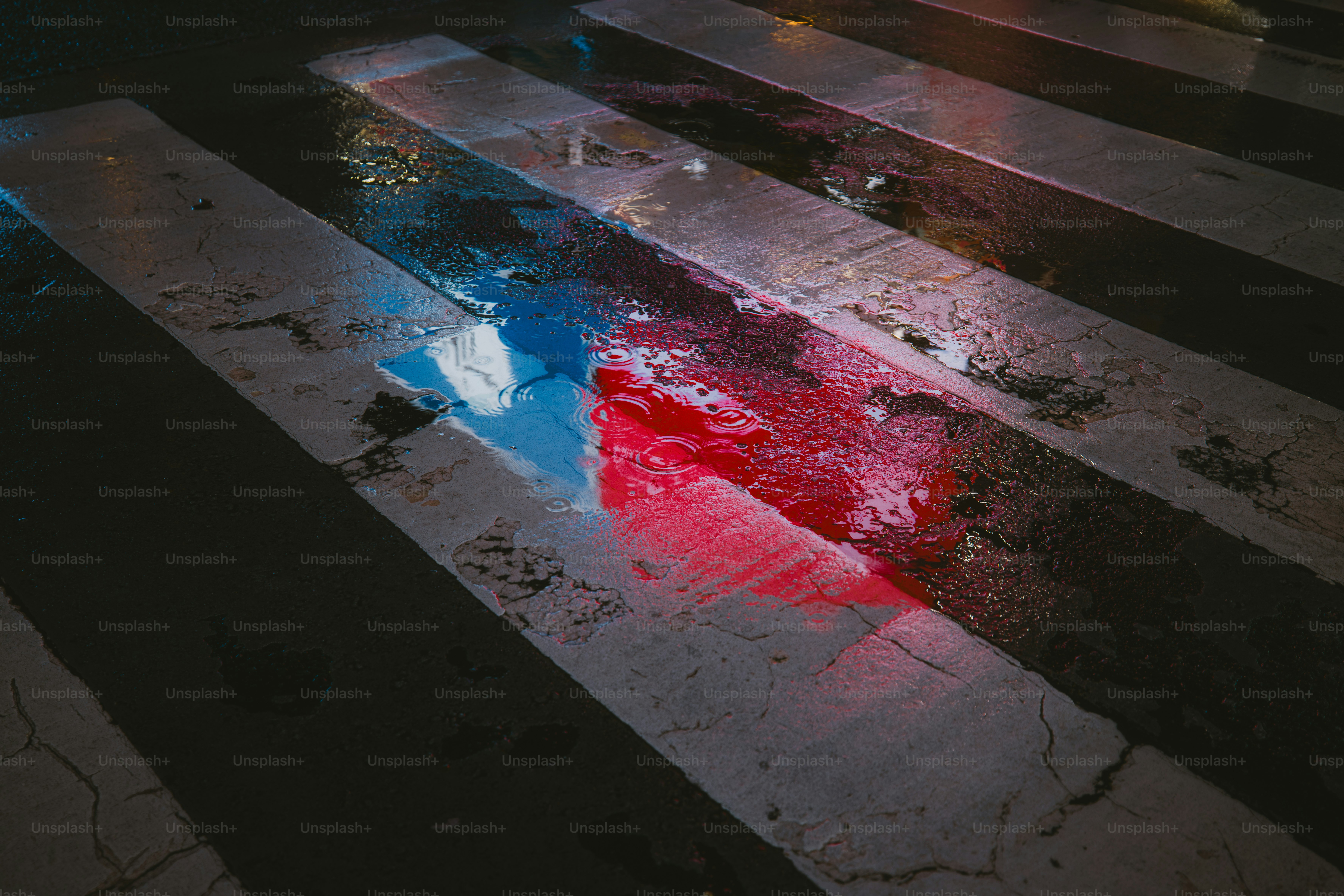 Raindrops falling into a puddle reflecting blue and red neon lights on a Shibuya crosswalk