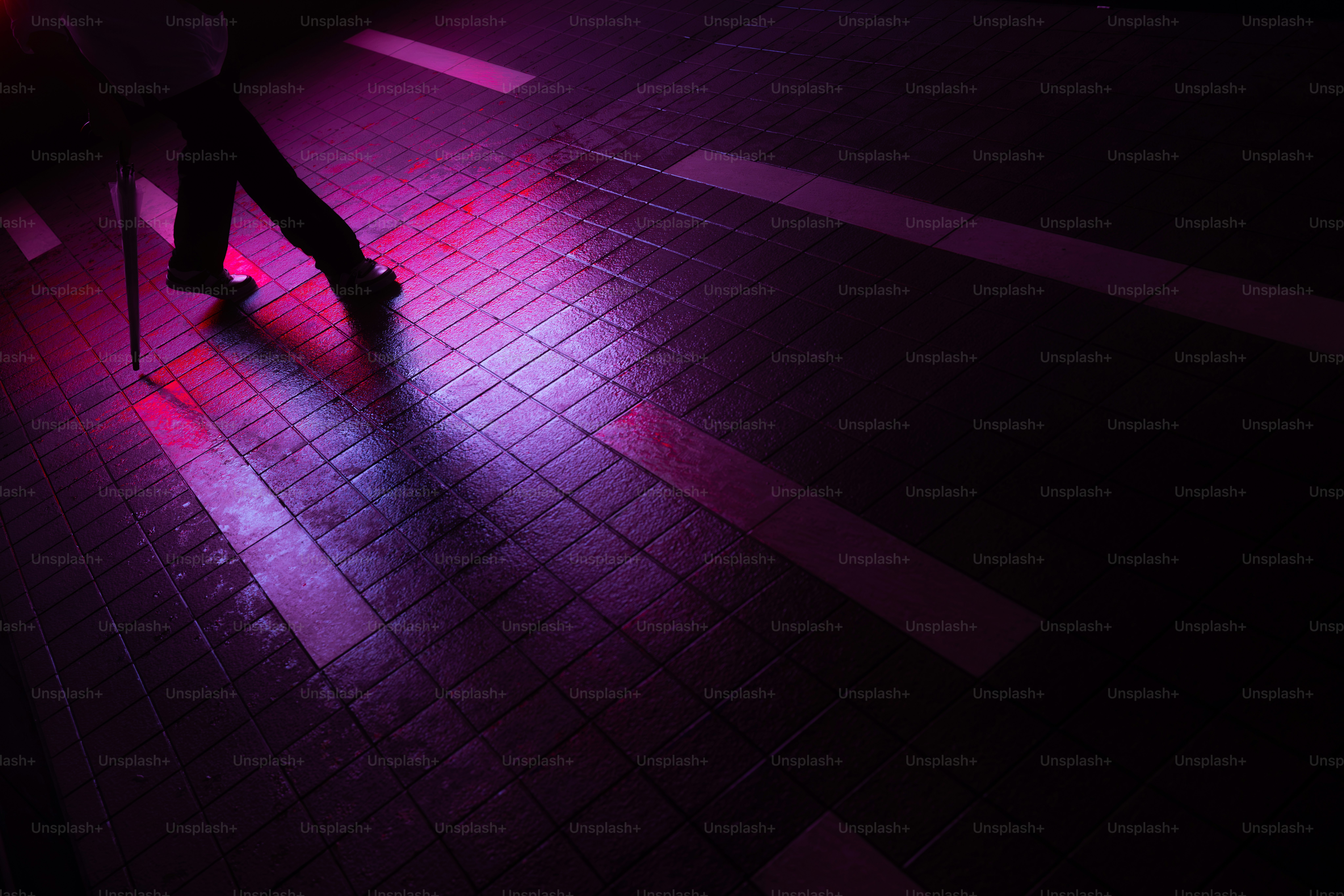 A person walking with an umbrella on a wet tiled surface under purple light