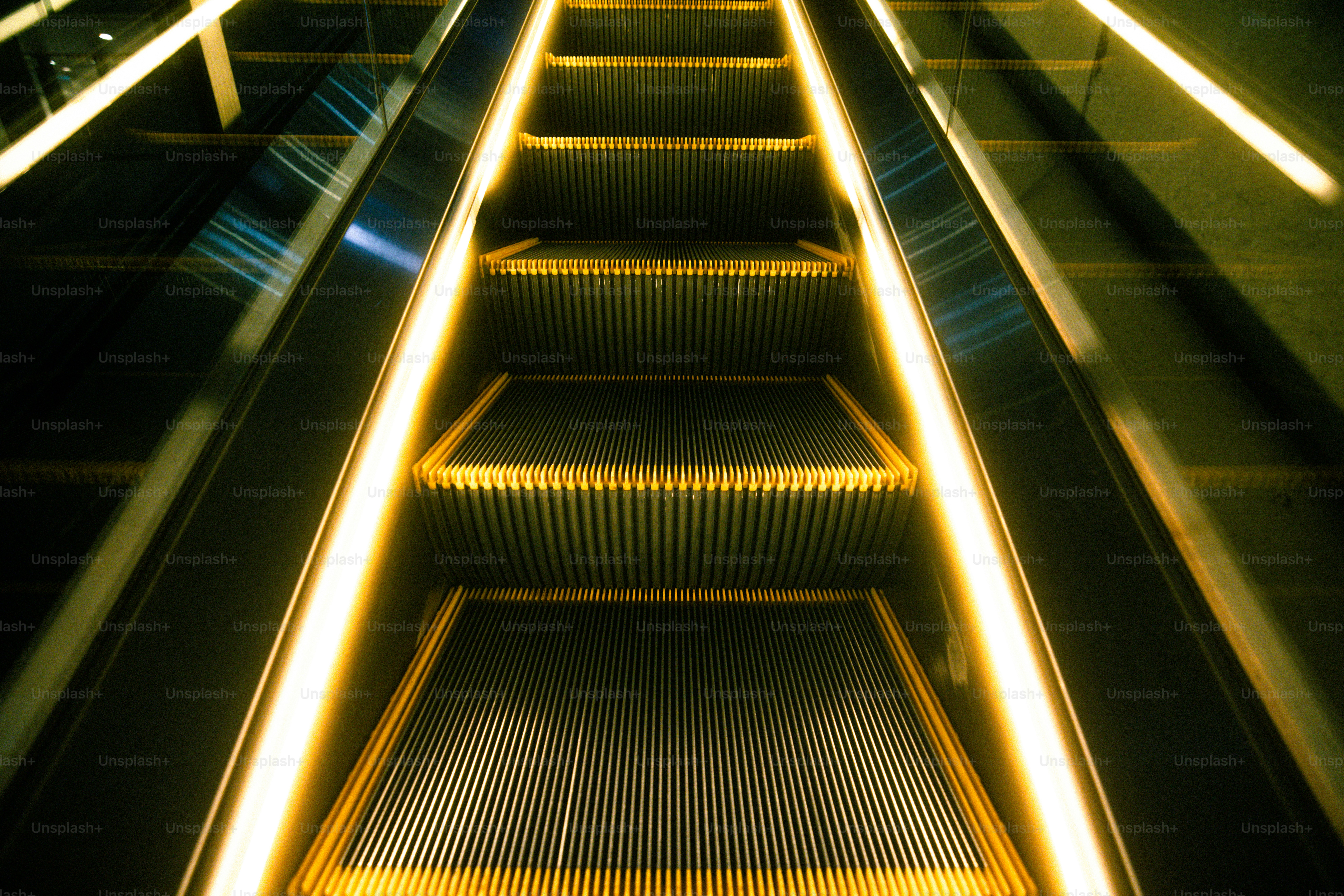 An upward view of an escalator with bright yellow illuminated handrails in Sumida City