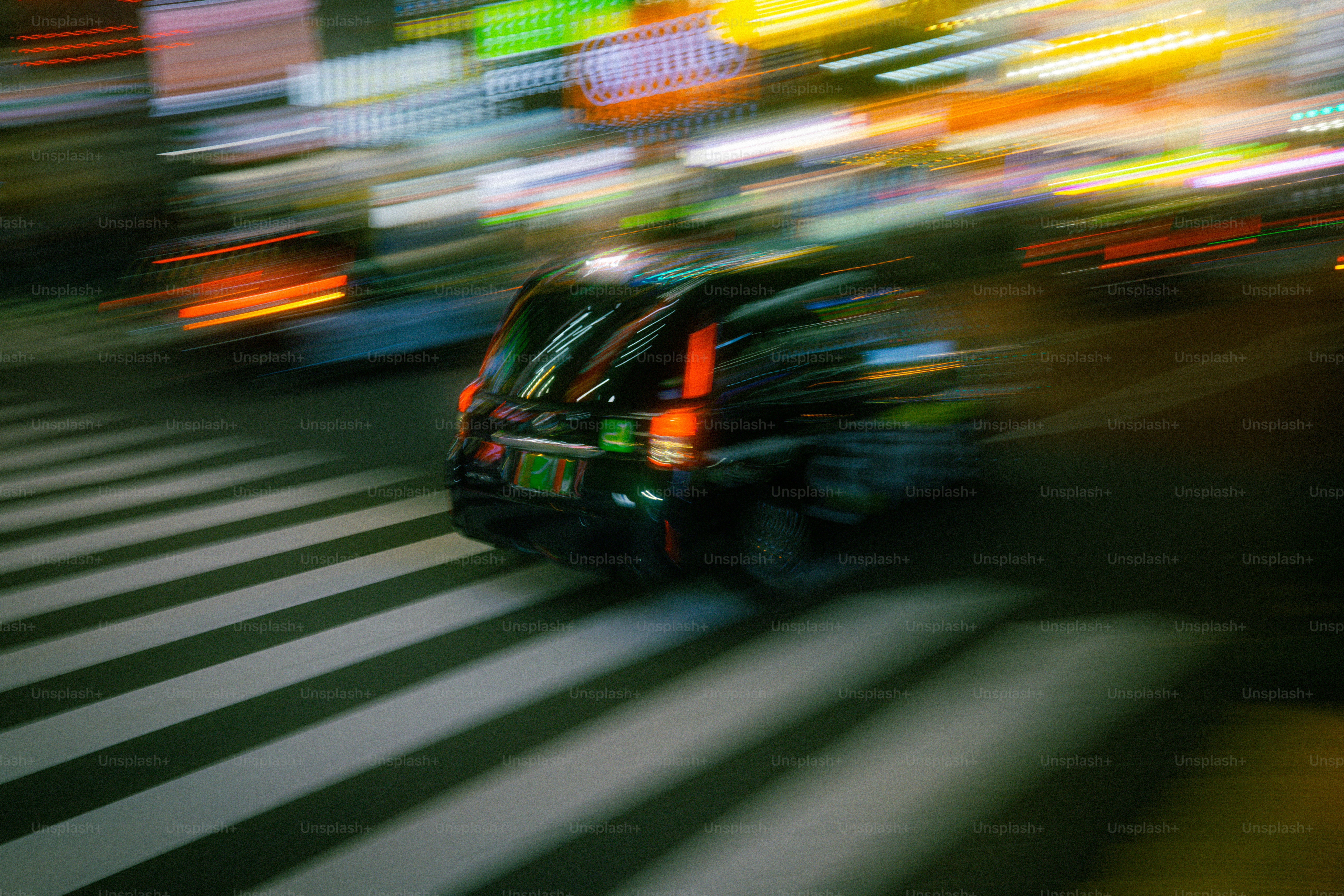 A black taxi driving across a pedestrian crossing at night with motion blur