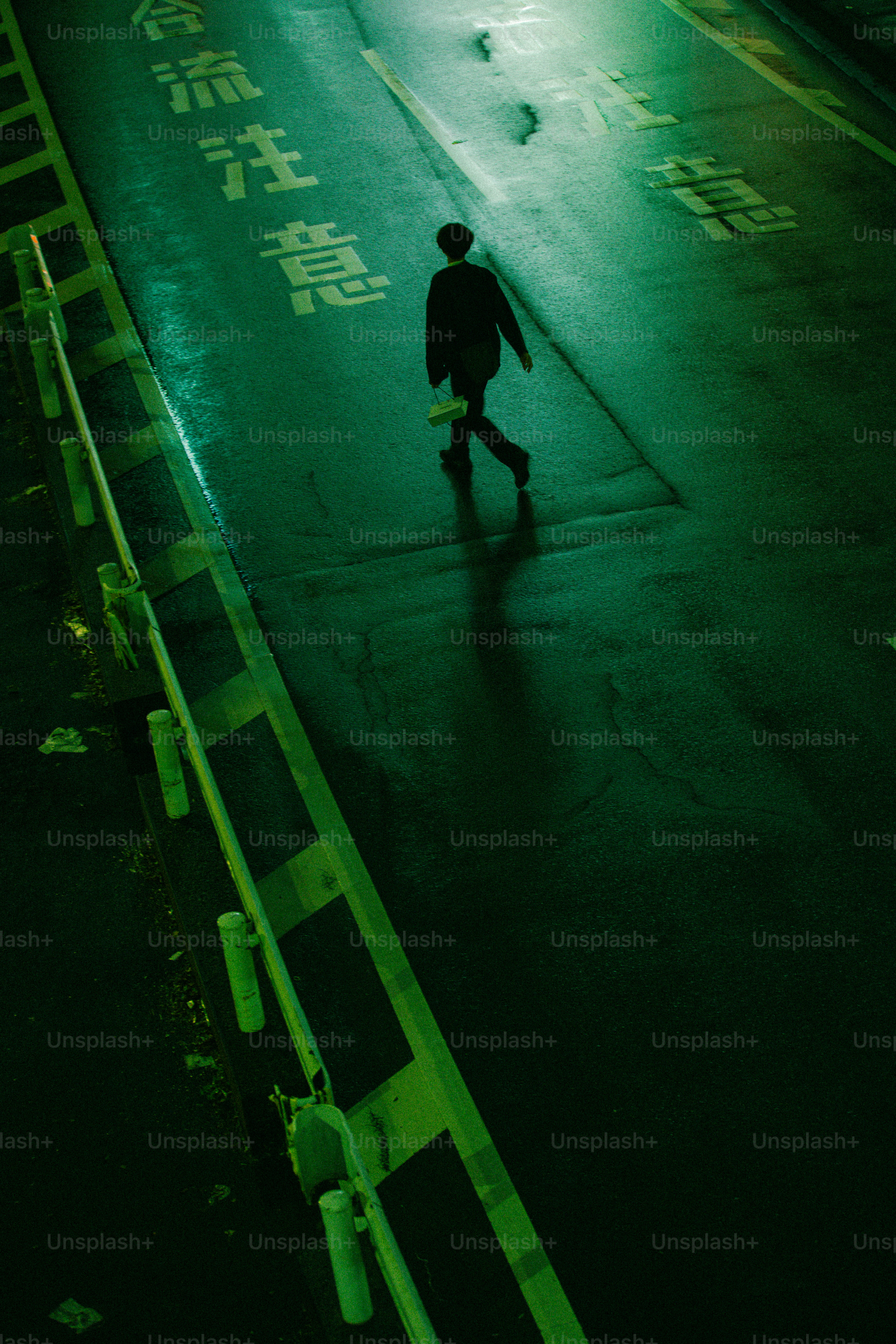 Una persona caminando por una carretera asfaltada mojada iluminada por luz verde por la noche