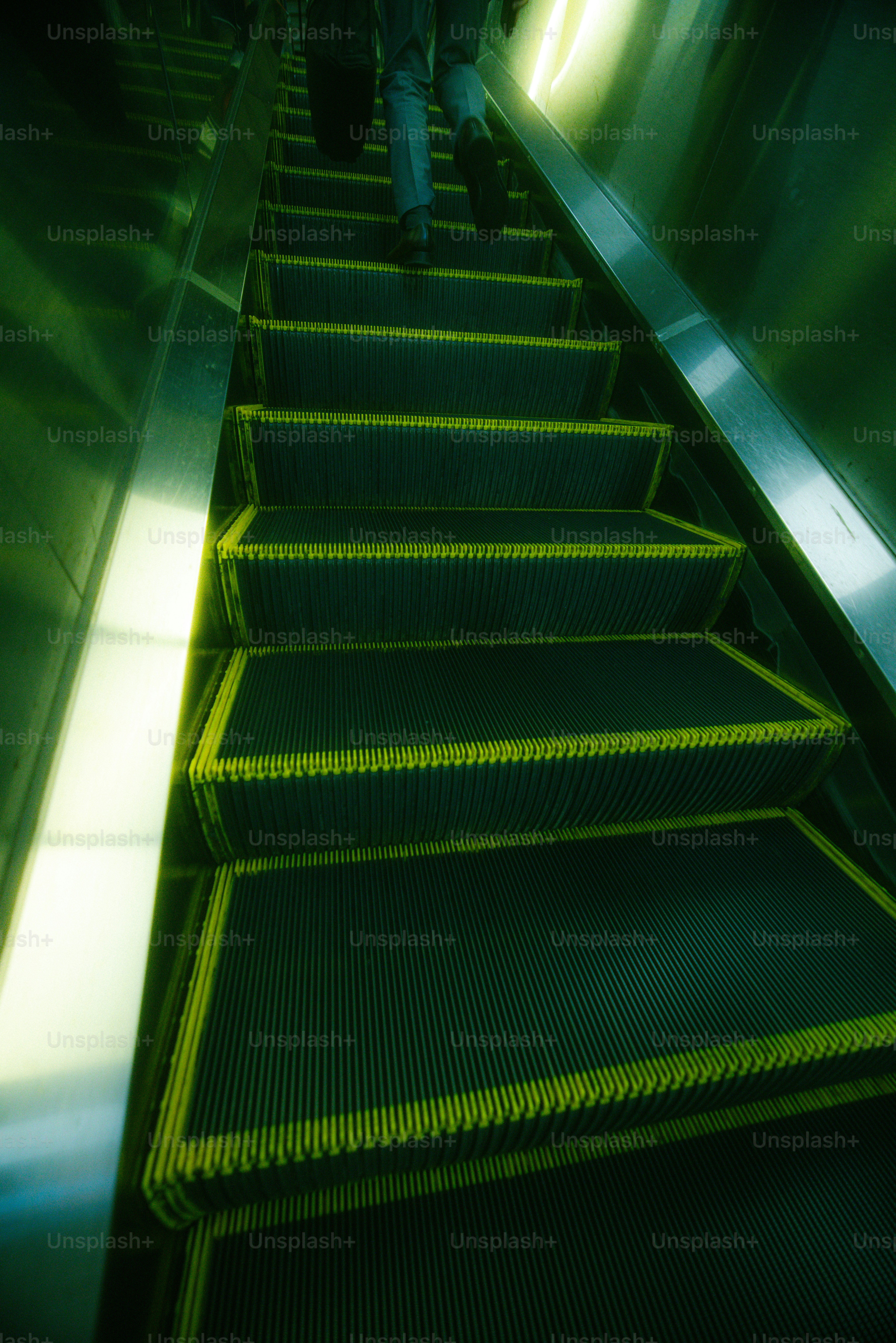 A person in trousers and dress shoes ascending an escalator in green light
