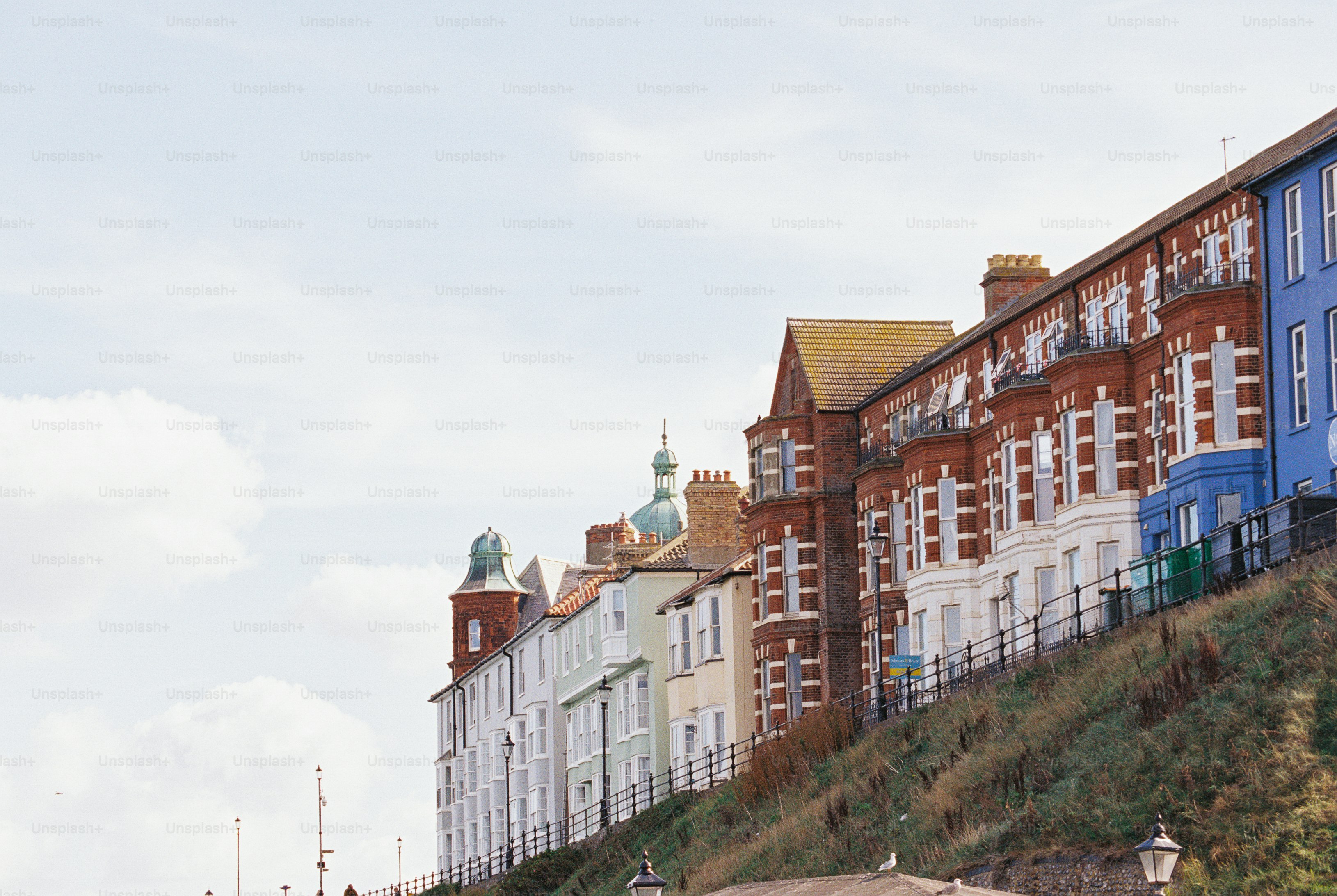 Seafront houses with red brick and pale facades lining a grassy slope behind iron railings