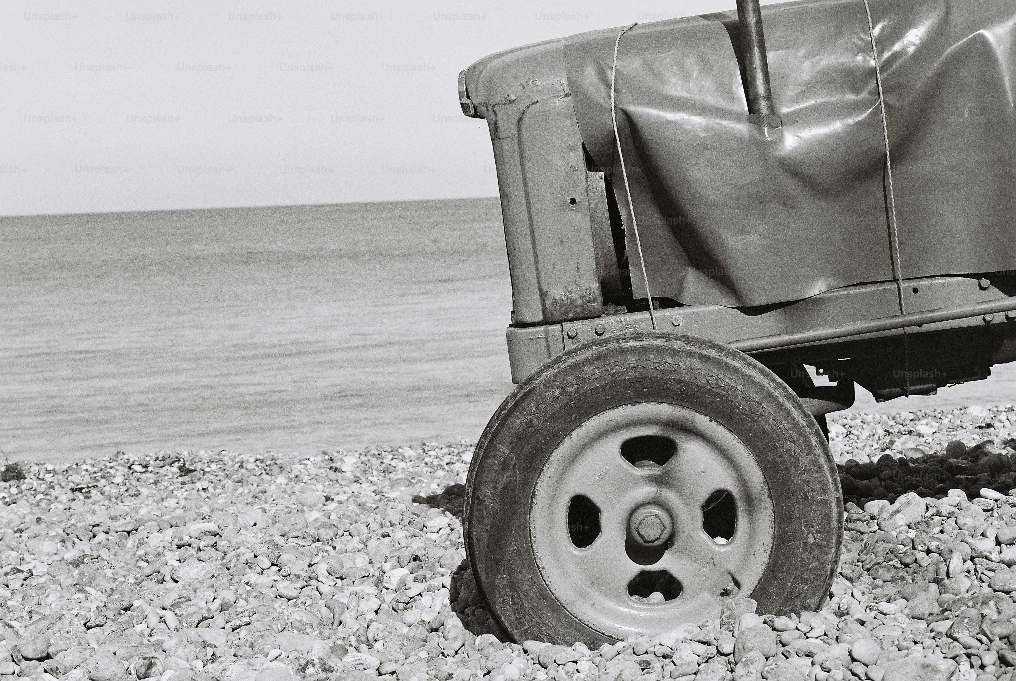 A black and white view of a tractor wheel on a shingle beach by the sea