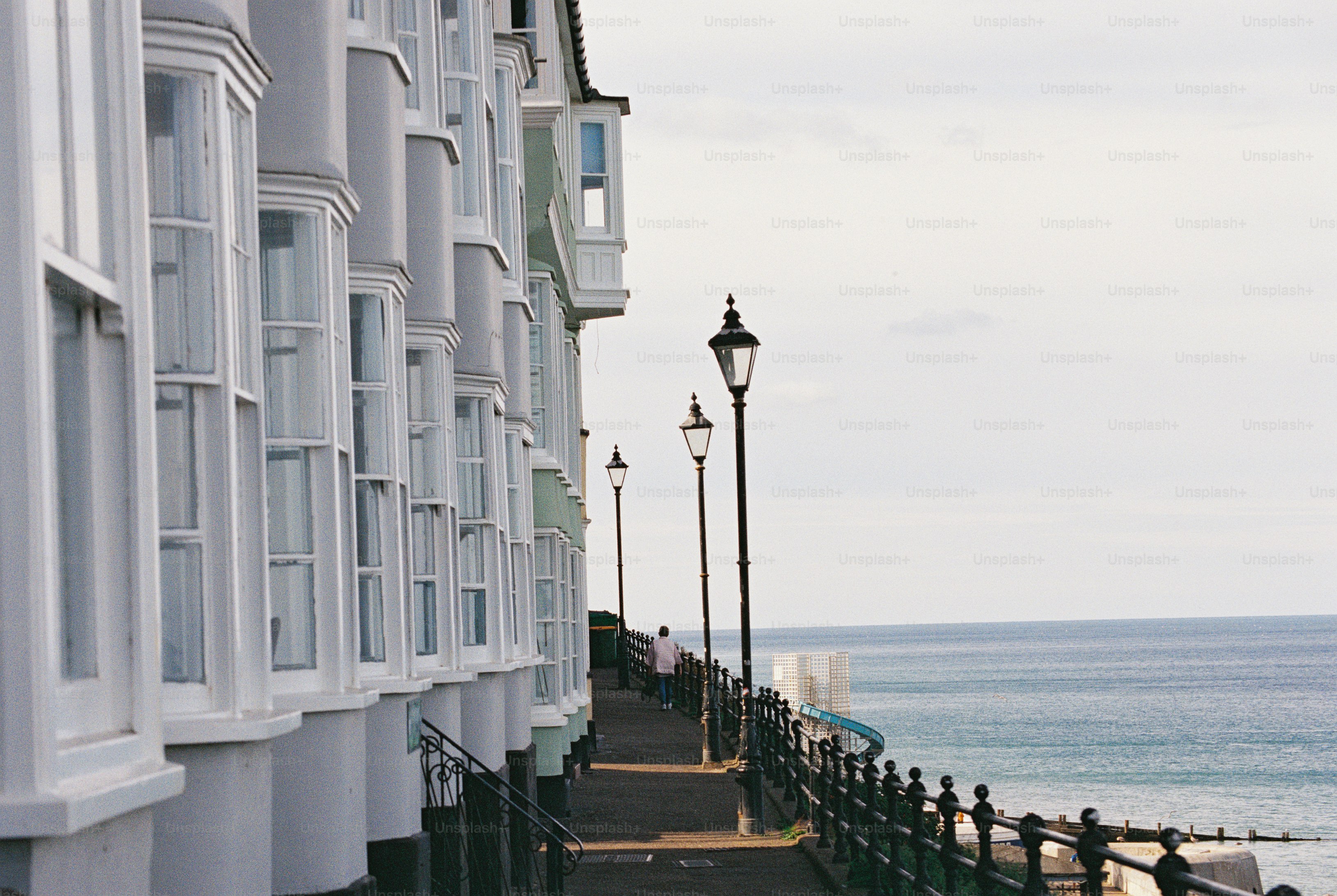 A person walking along a seafront path beside a terrace of white houses with sash bay windows