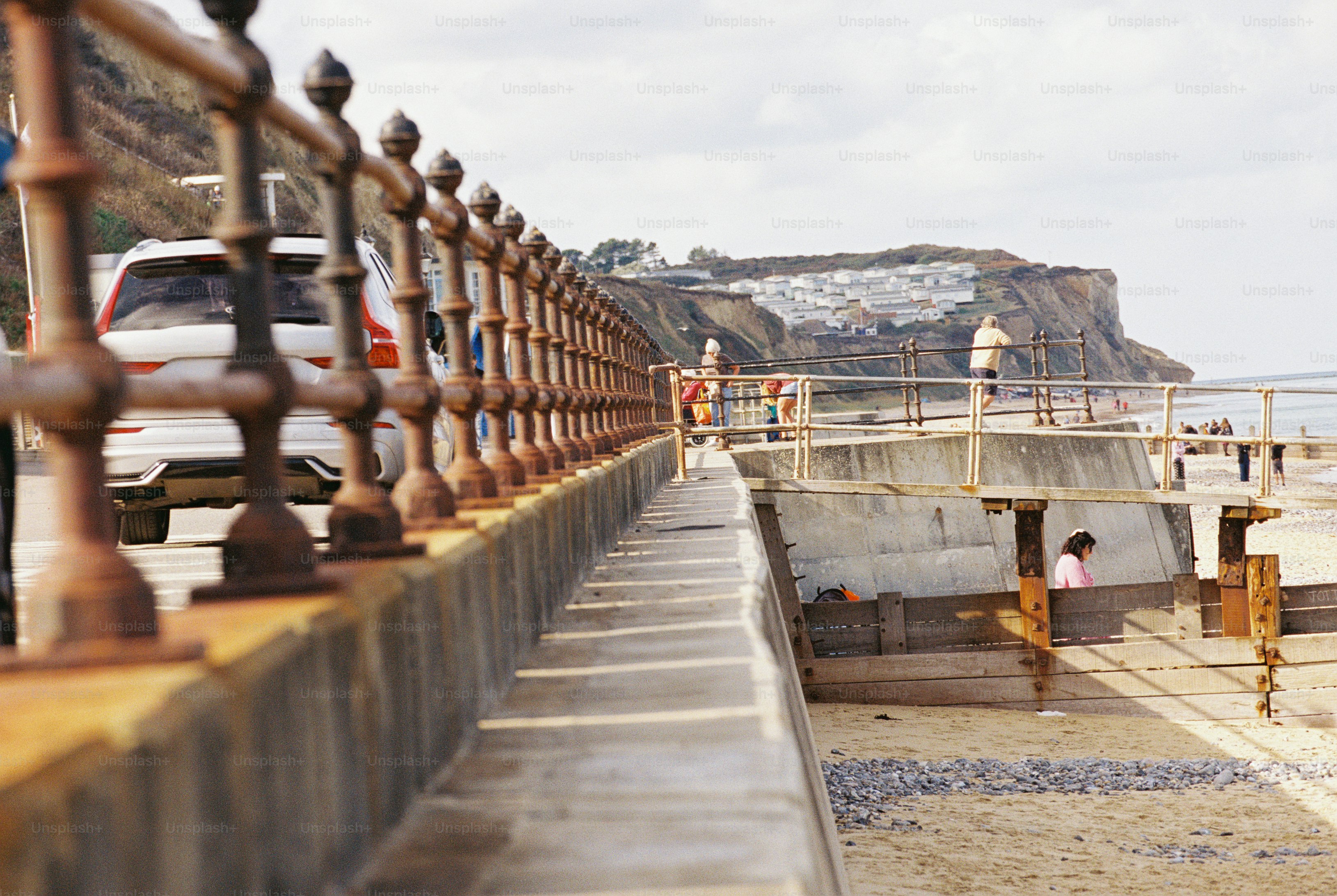 A row of rust-brown cast iron balusters with acorn finials along a sea wall beside a beach