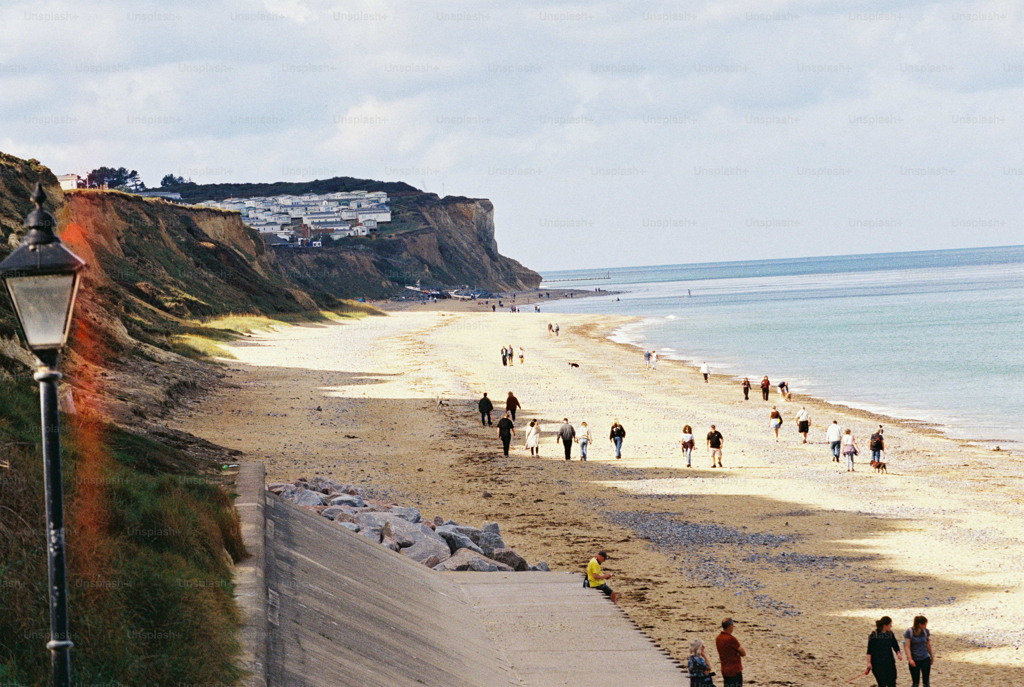 People walking along a sandy beach below eroded cliffs topped with white caravans
