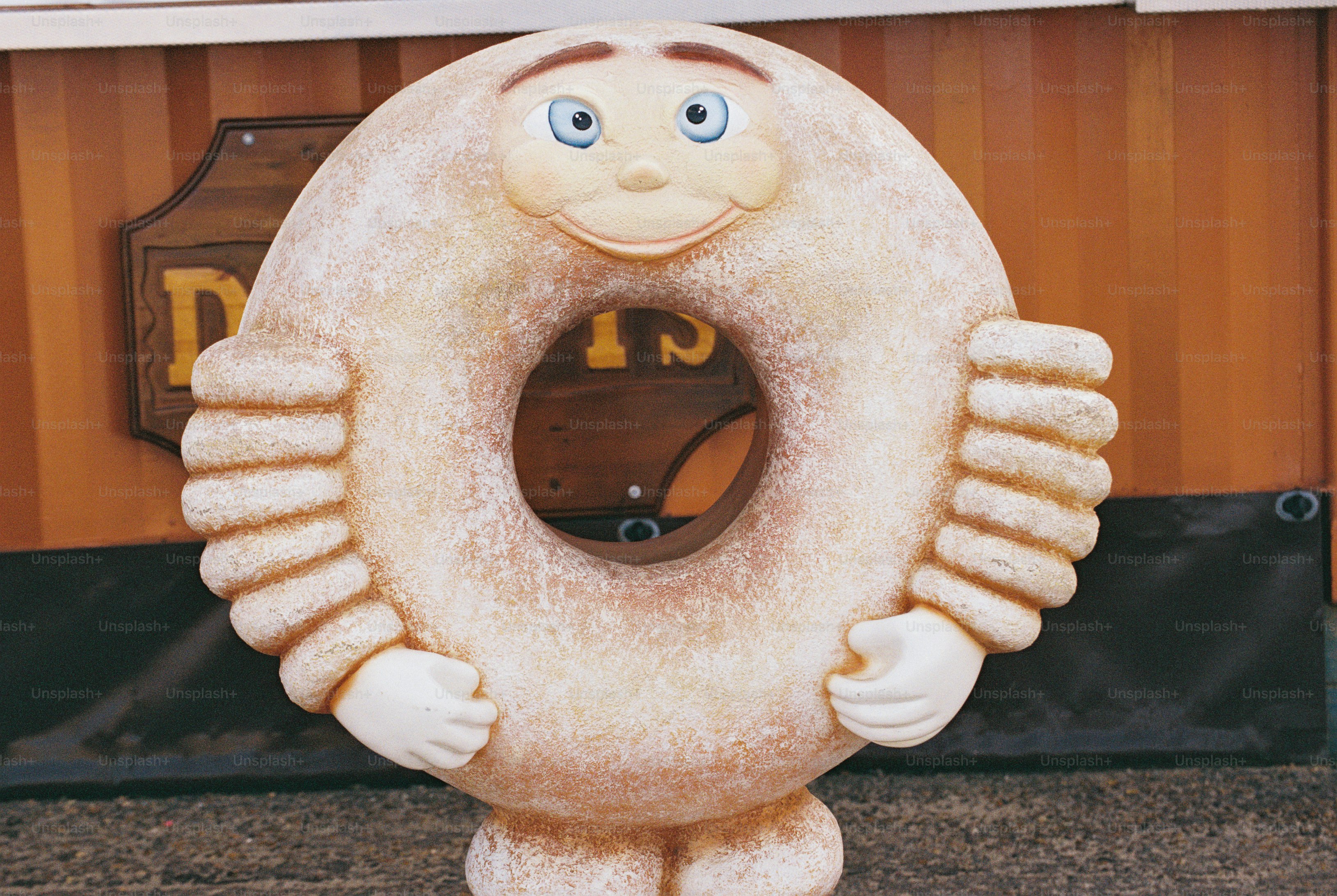 A doughnut-shaped sculpture with a smiling face and white gloved hands in front of an orange stall