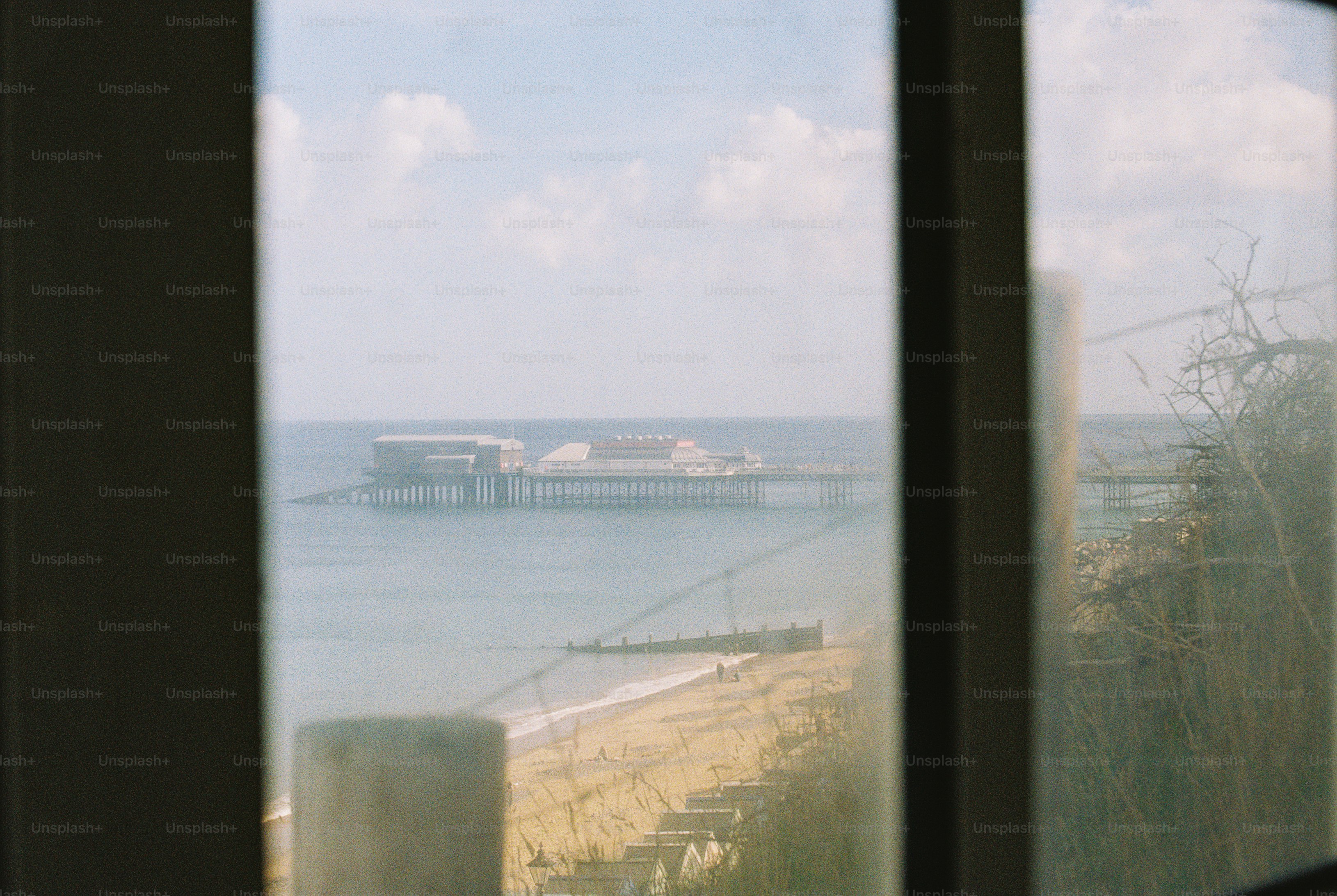 Cromer Pier on a pale blue sea viewed through a window with dry grasses