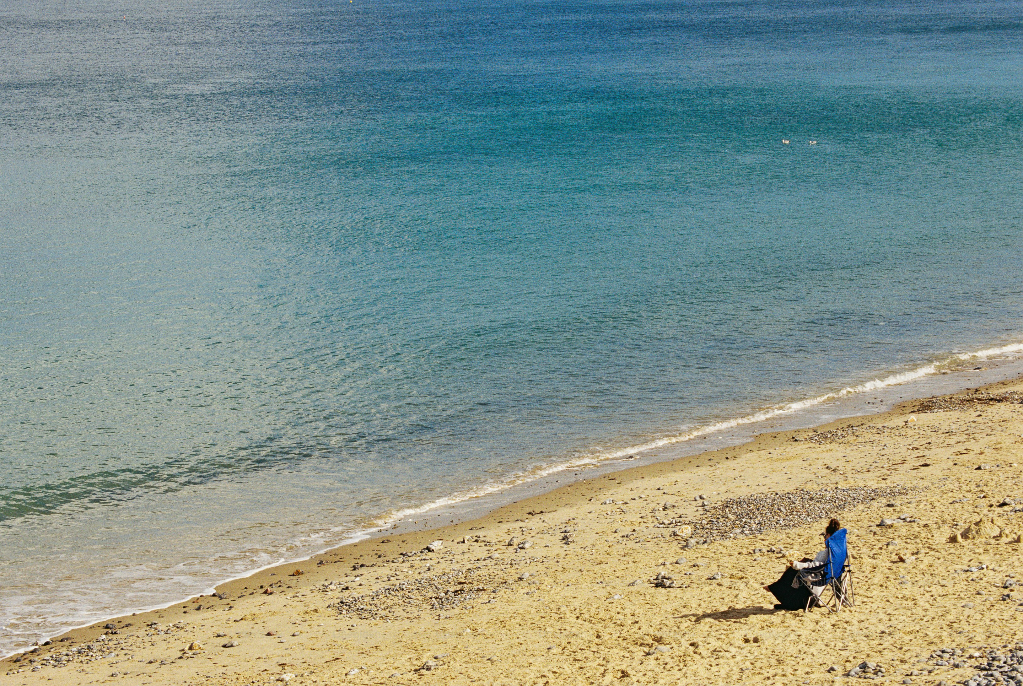 A person in a blue folding chair on a sandy beach overlooking turquoise water