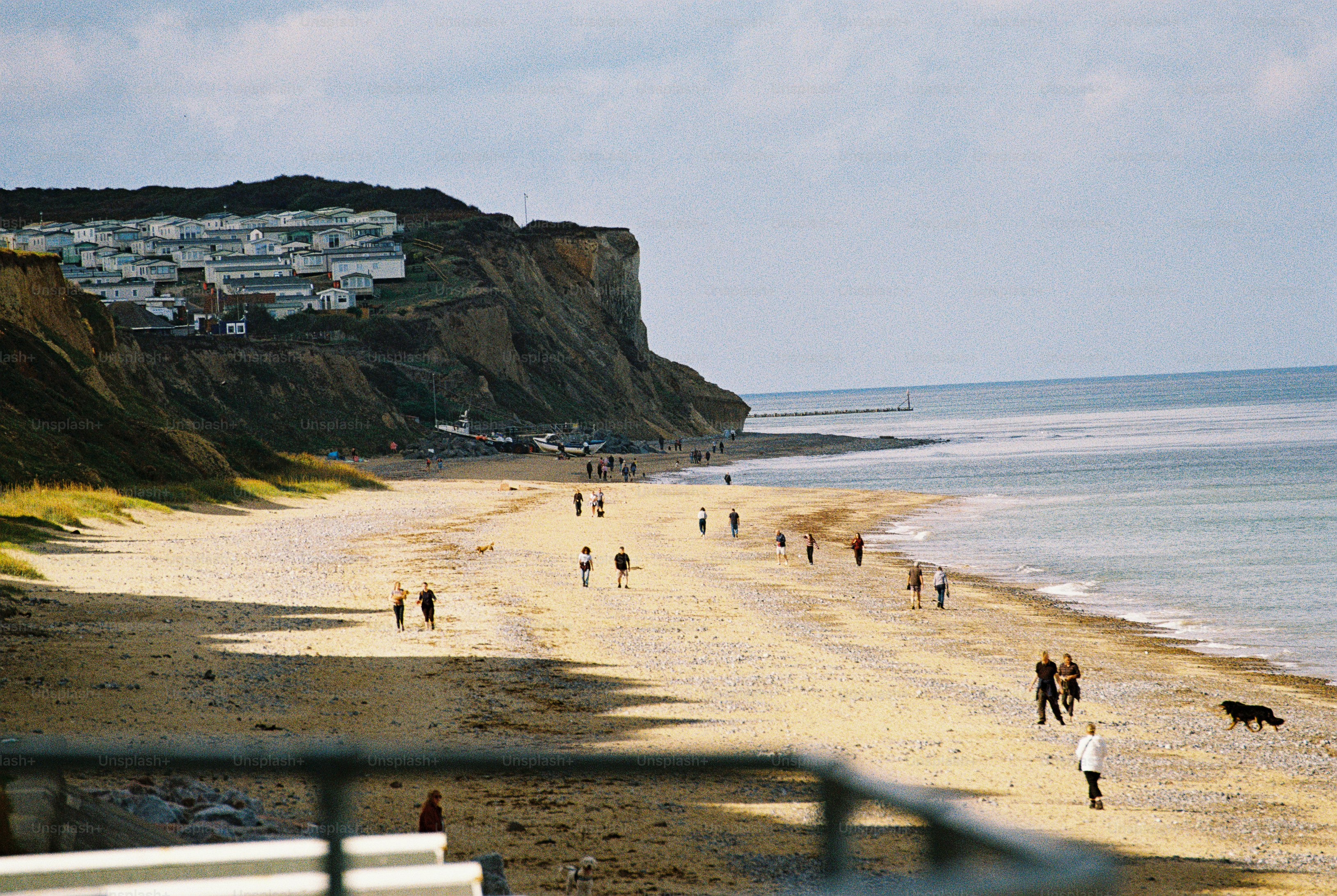People walking and running along a sunlit beach below a cliff topped with caravans