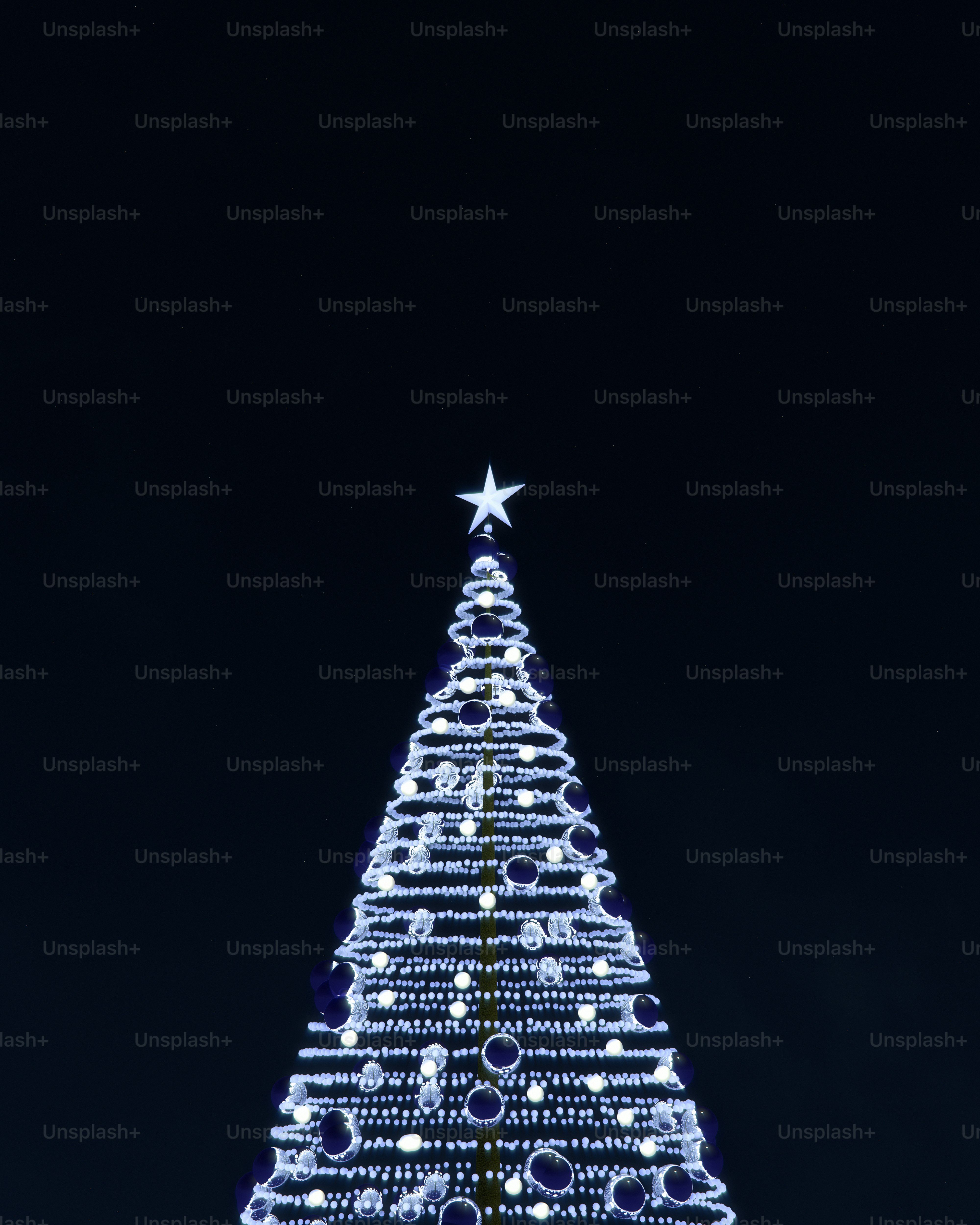 A Christmas tree decorated with glowing white lights and dark ornaments against black