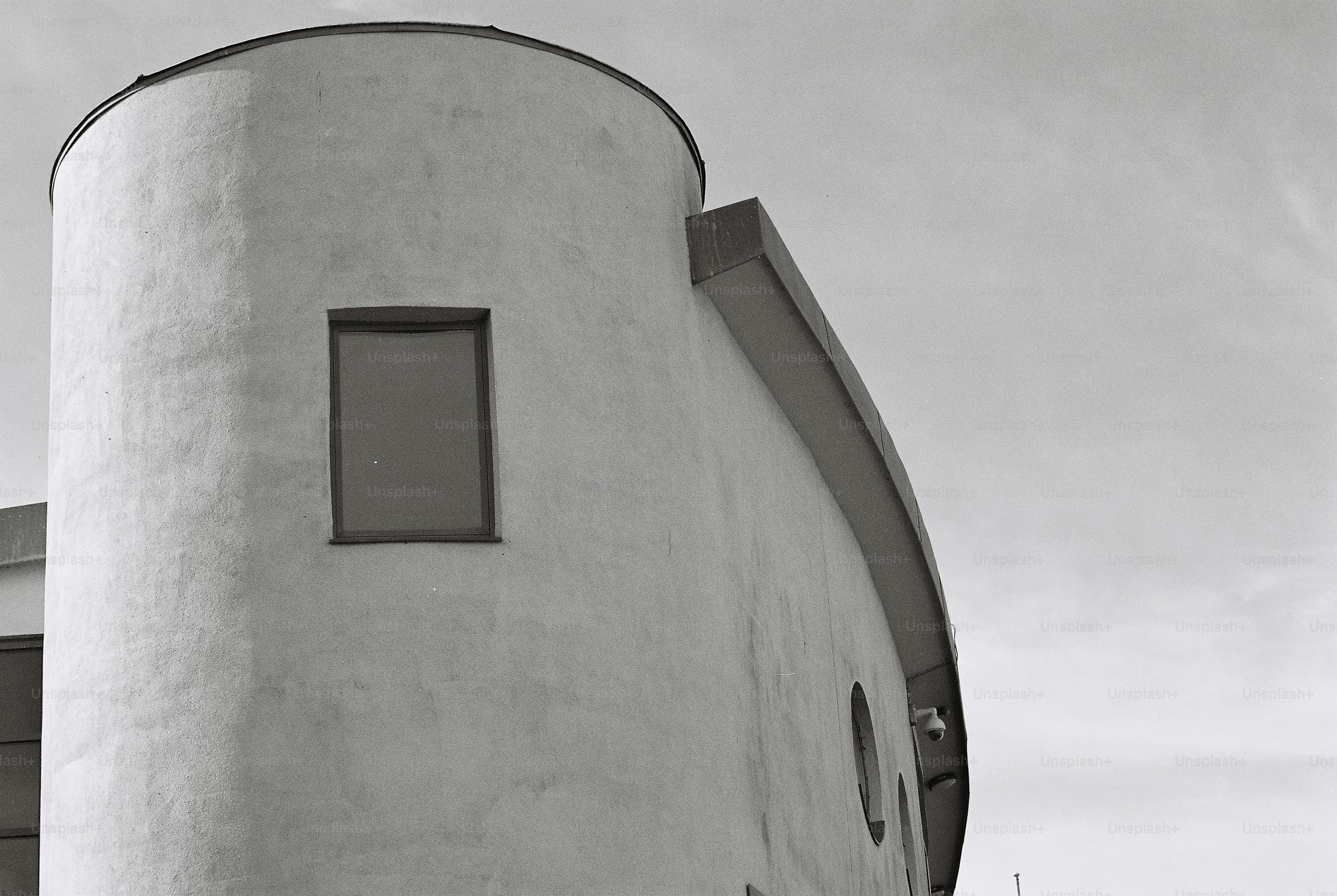 A curved concrete building with a rectangular window and two round porthole windows