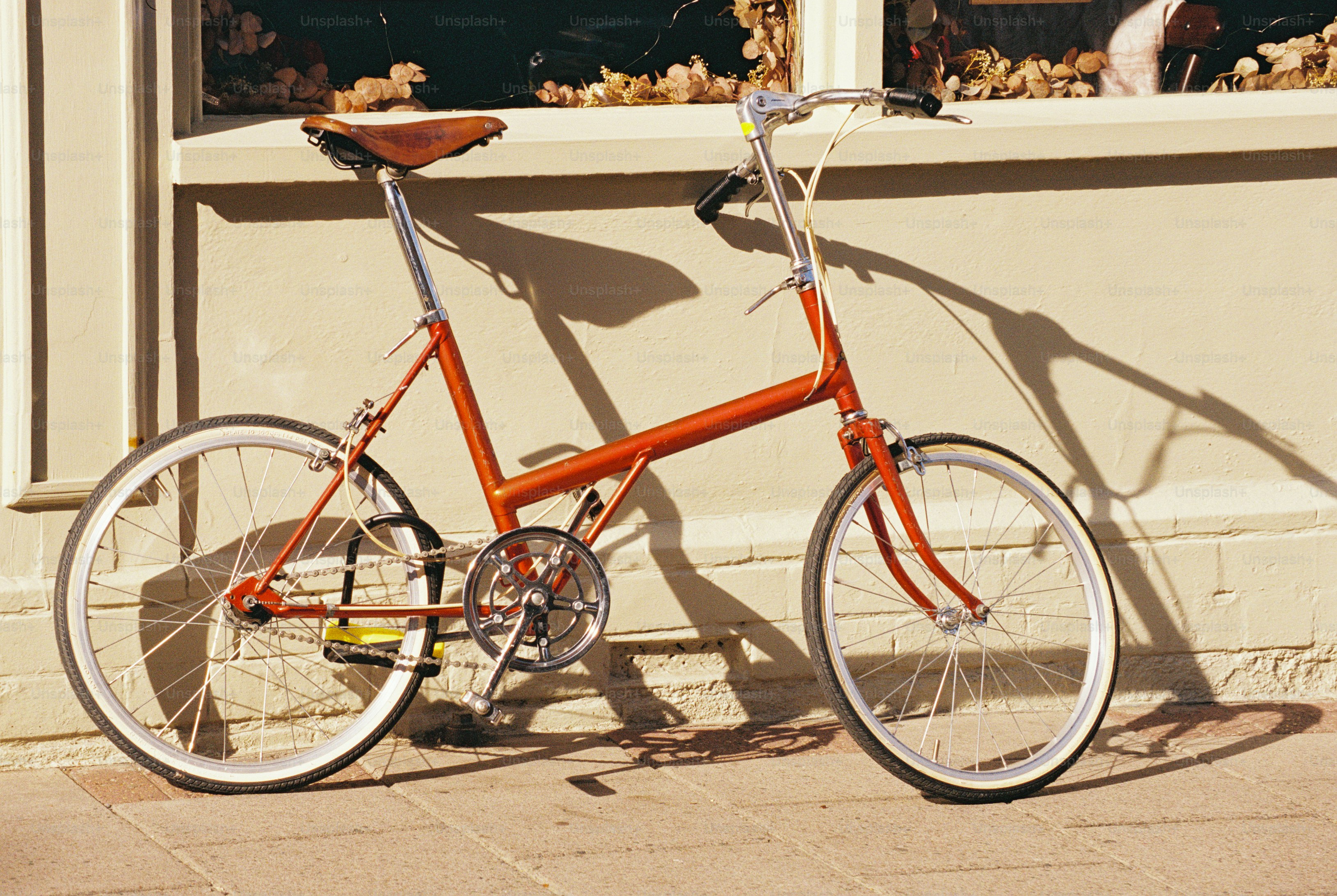A small red bicycle with a brown leather saddle against a cream wall