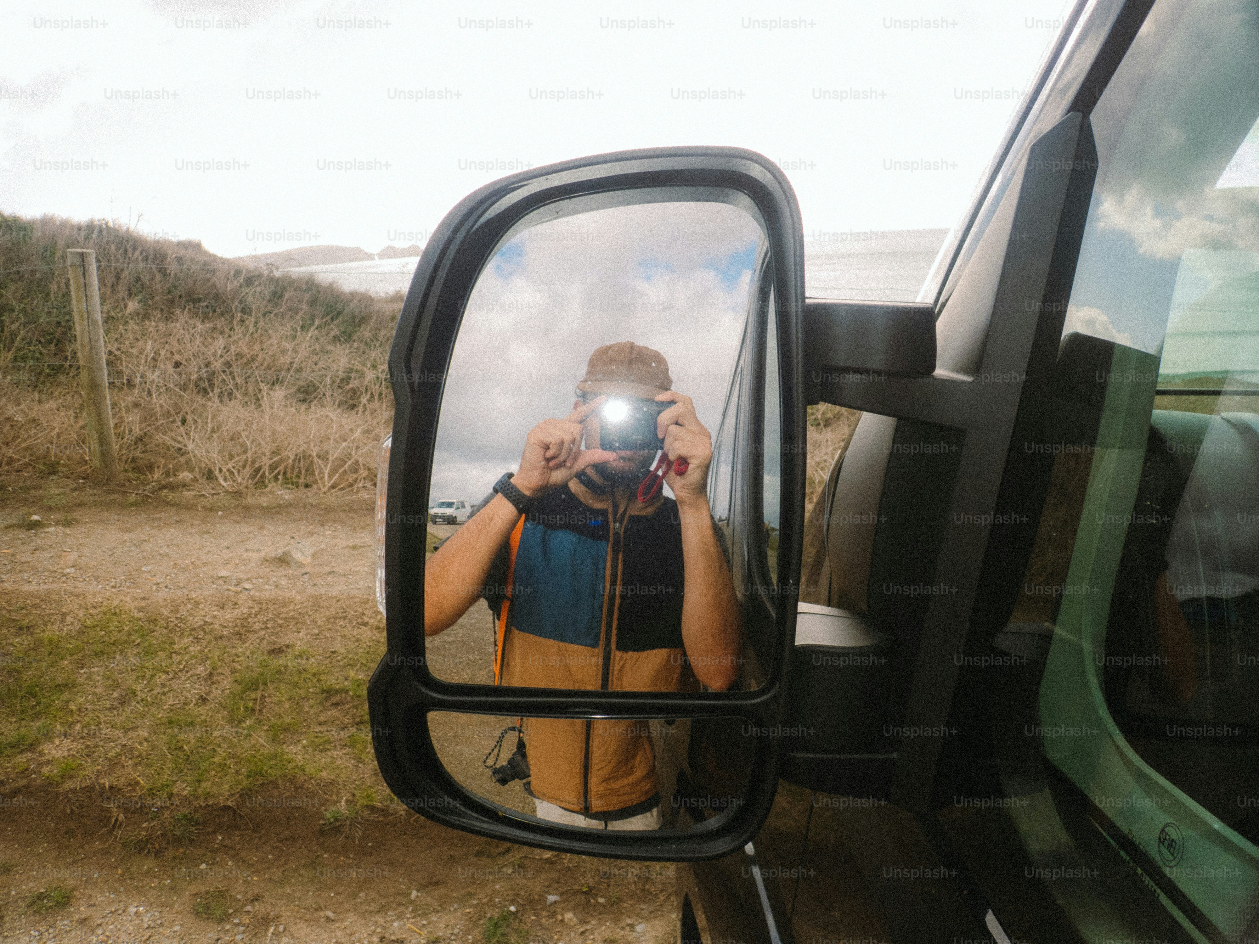 A person in a color-blocked vest taking a photo in a vehicle side mirror