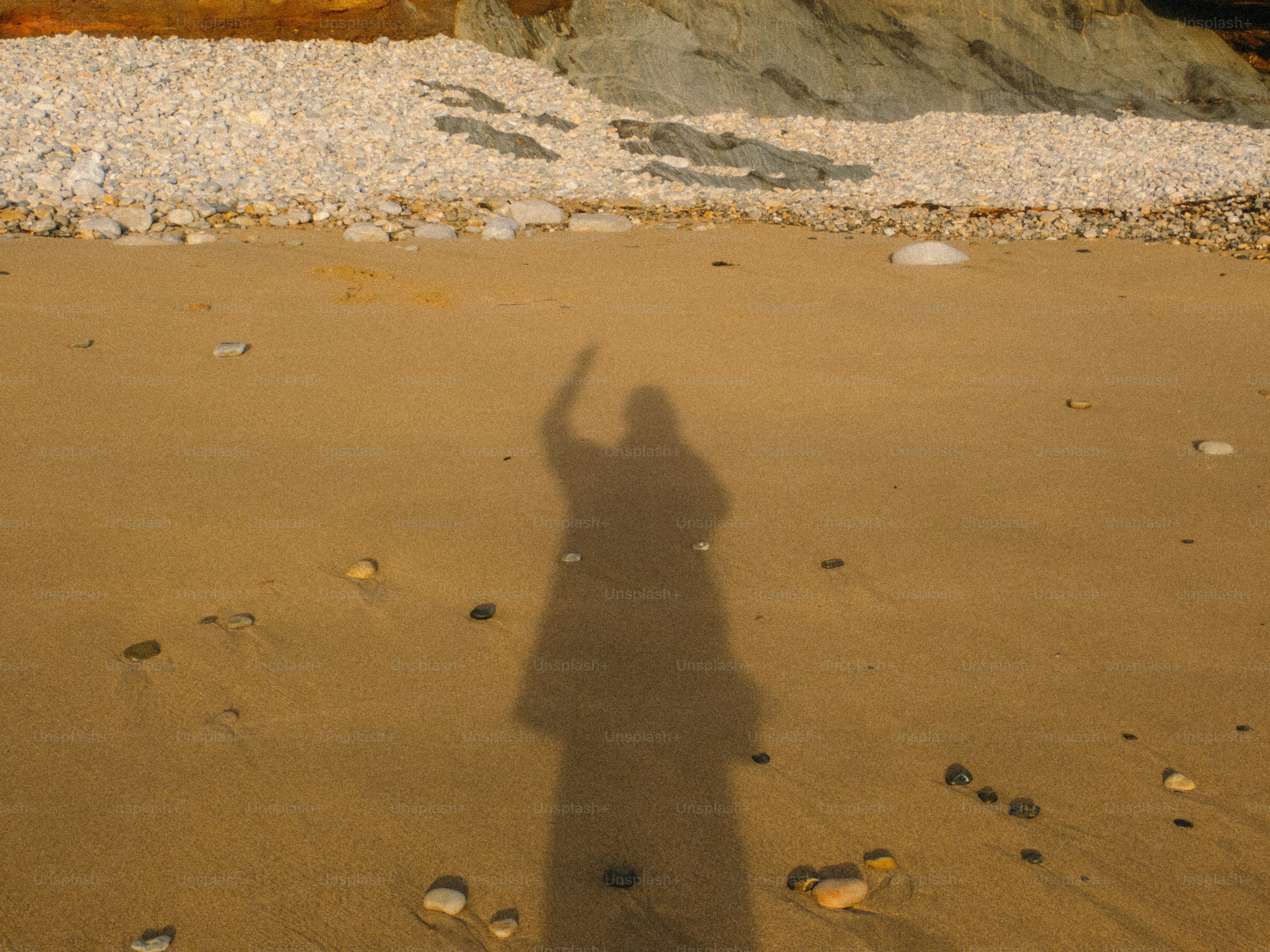 The shadow of a person with one arm raised on a sandy beach
