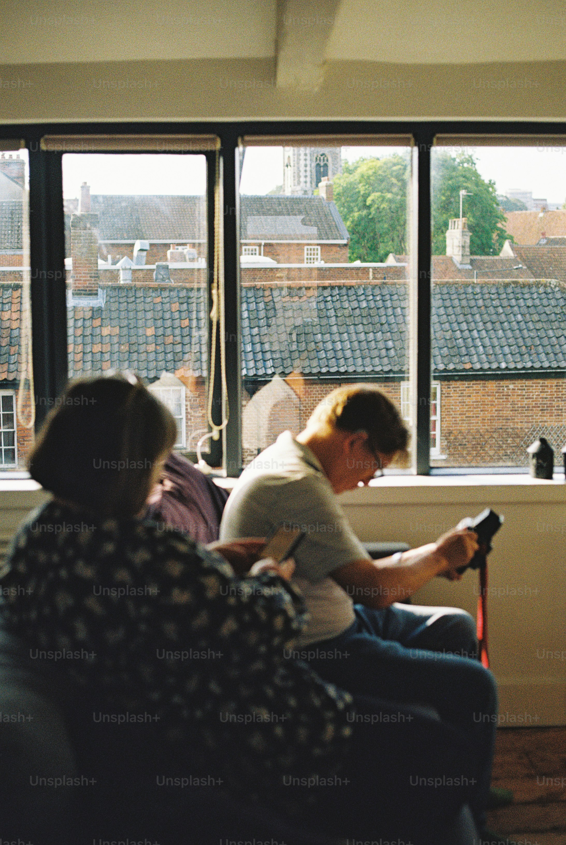Two people sitting on a sofa in front of a window overlooking brick rooftops