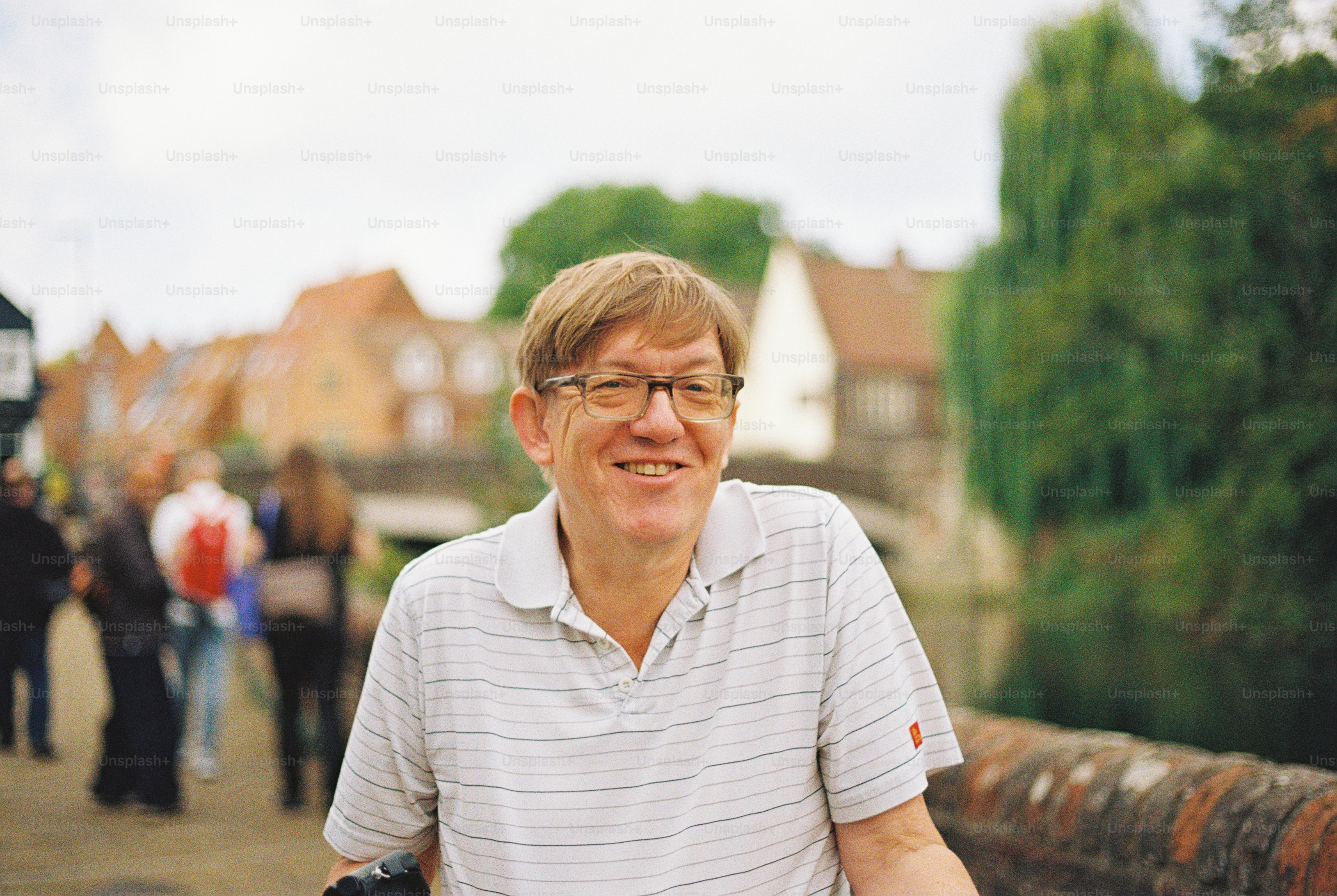 A smiling man with glasses in a striped polo shirt outdoors