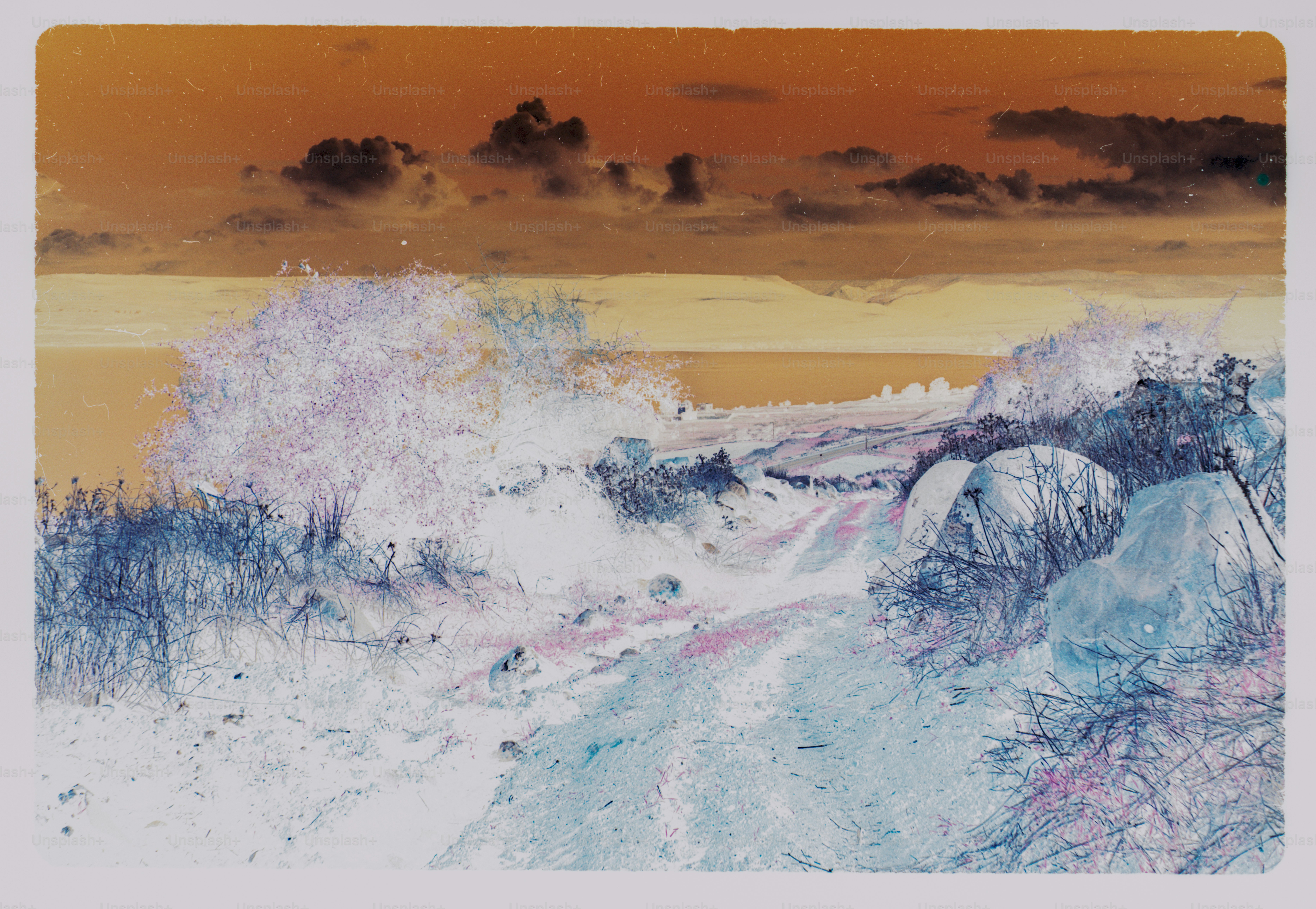A dirt path winding through a rocky landscape under a dark orange sky