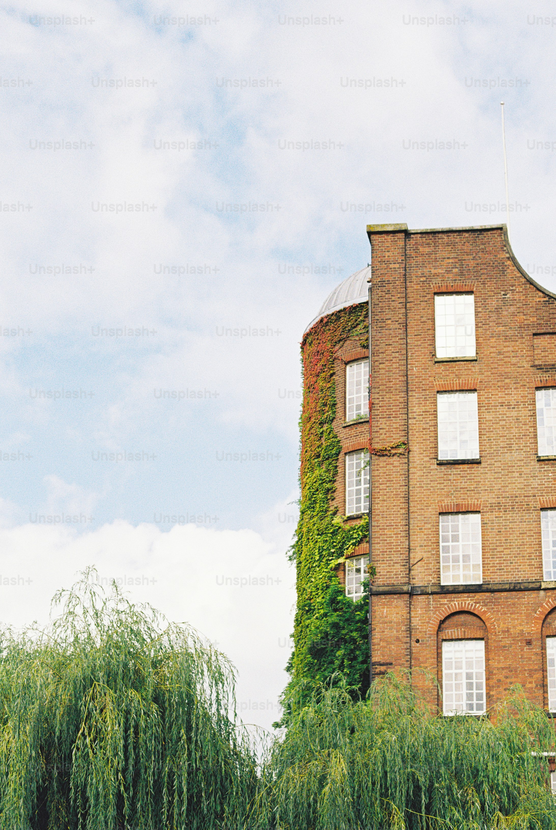 A brick building with a curved wall covered in green ivy under a cloudy sky