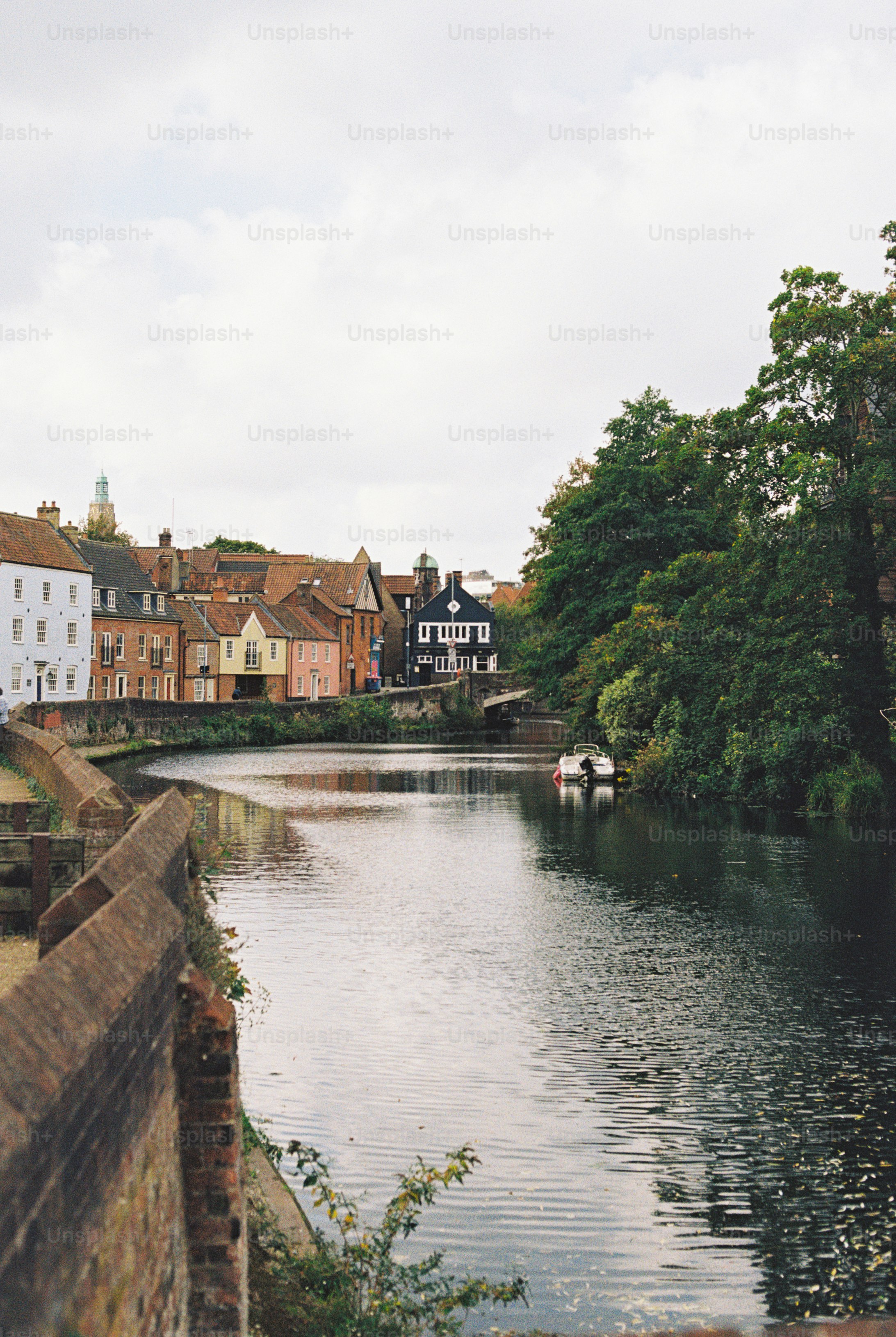 A calm river flowing past historic colorful houses and lush trees in Norwich