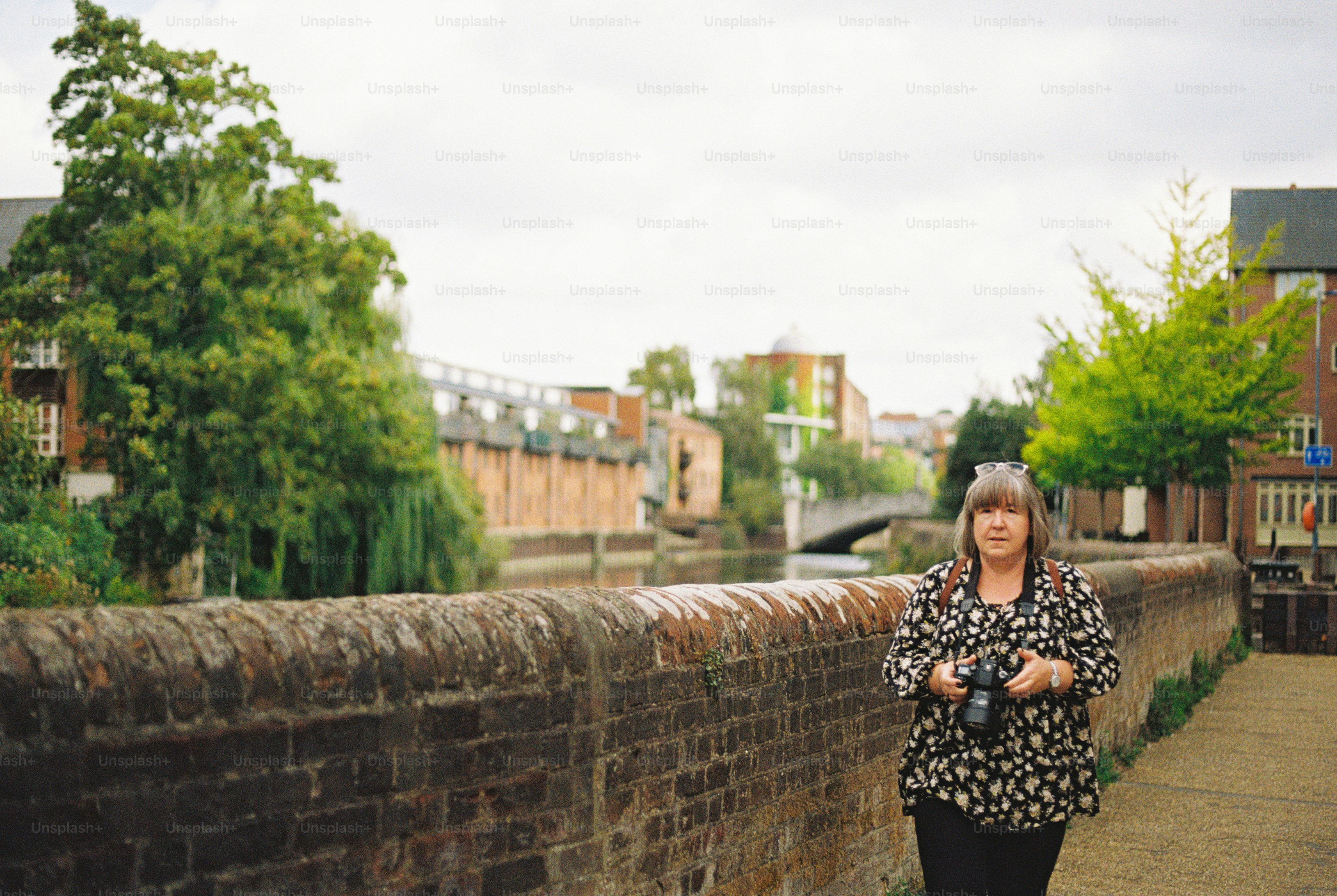 A woman holding a camera walking along a brick wall beside a canal