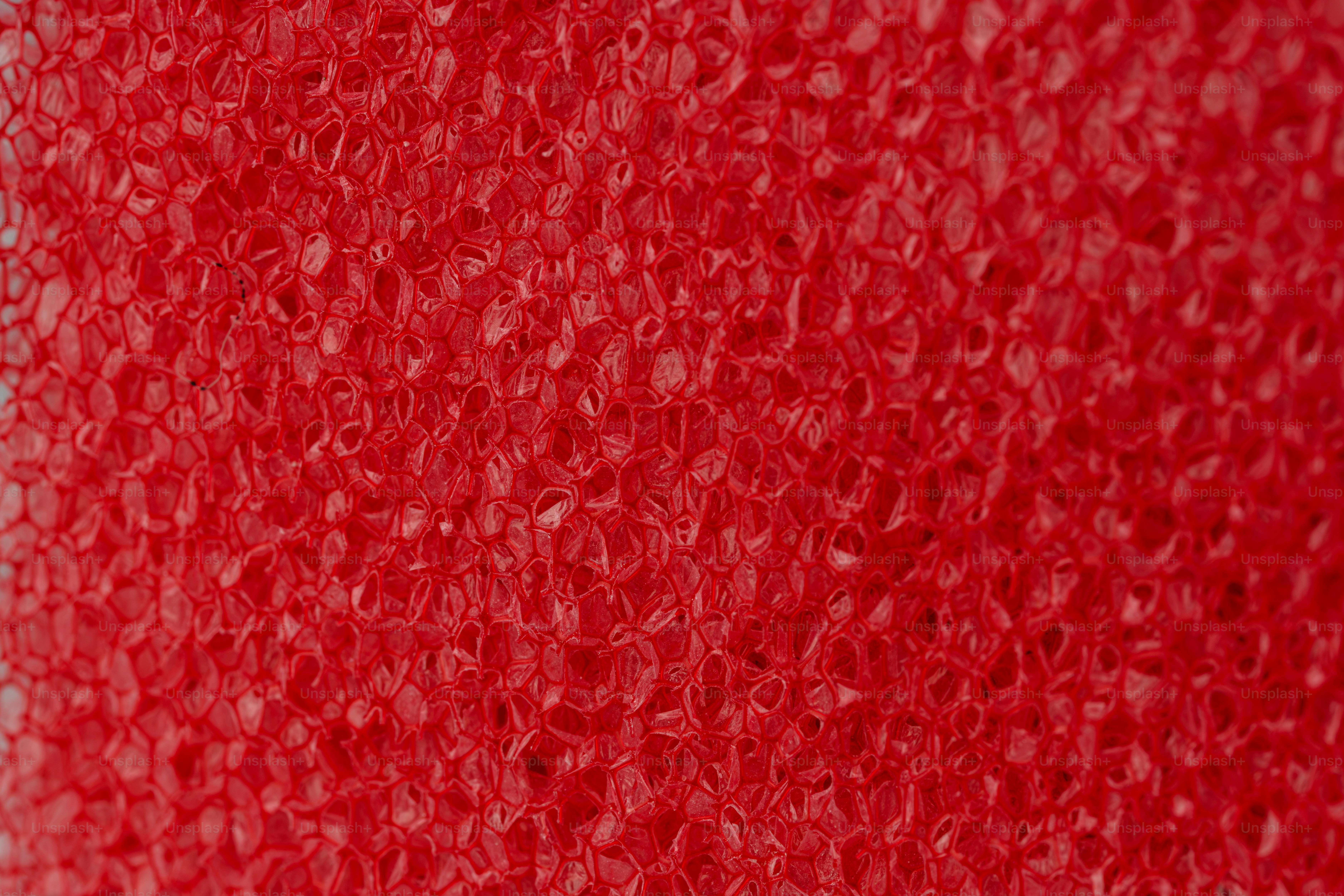 A close-up of a red porous foam texture with irregular honeycomb cells