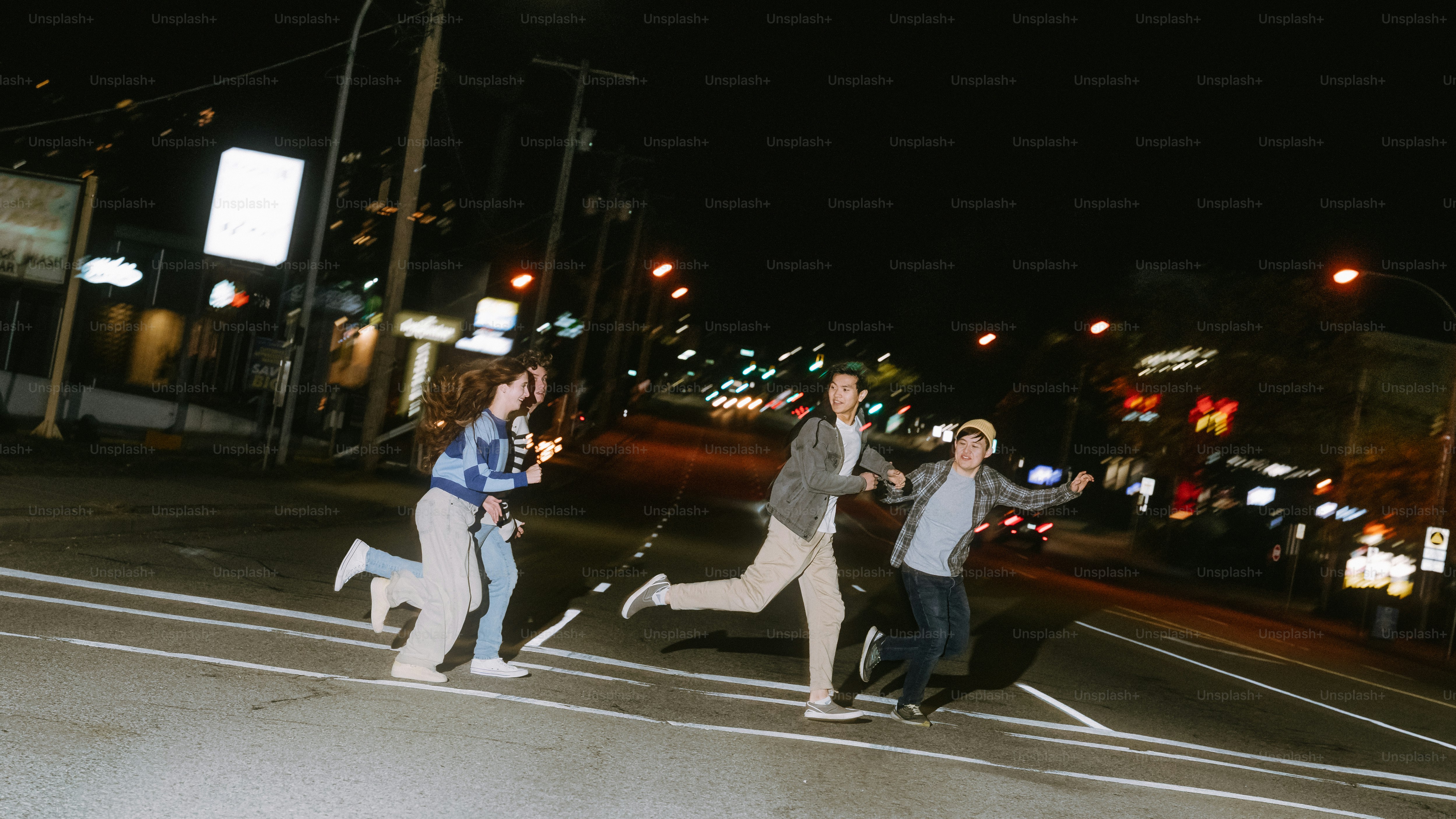 Four people running across a city street at night under bright streetlights