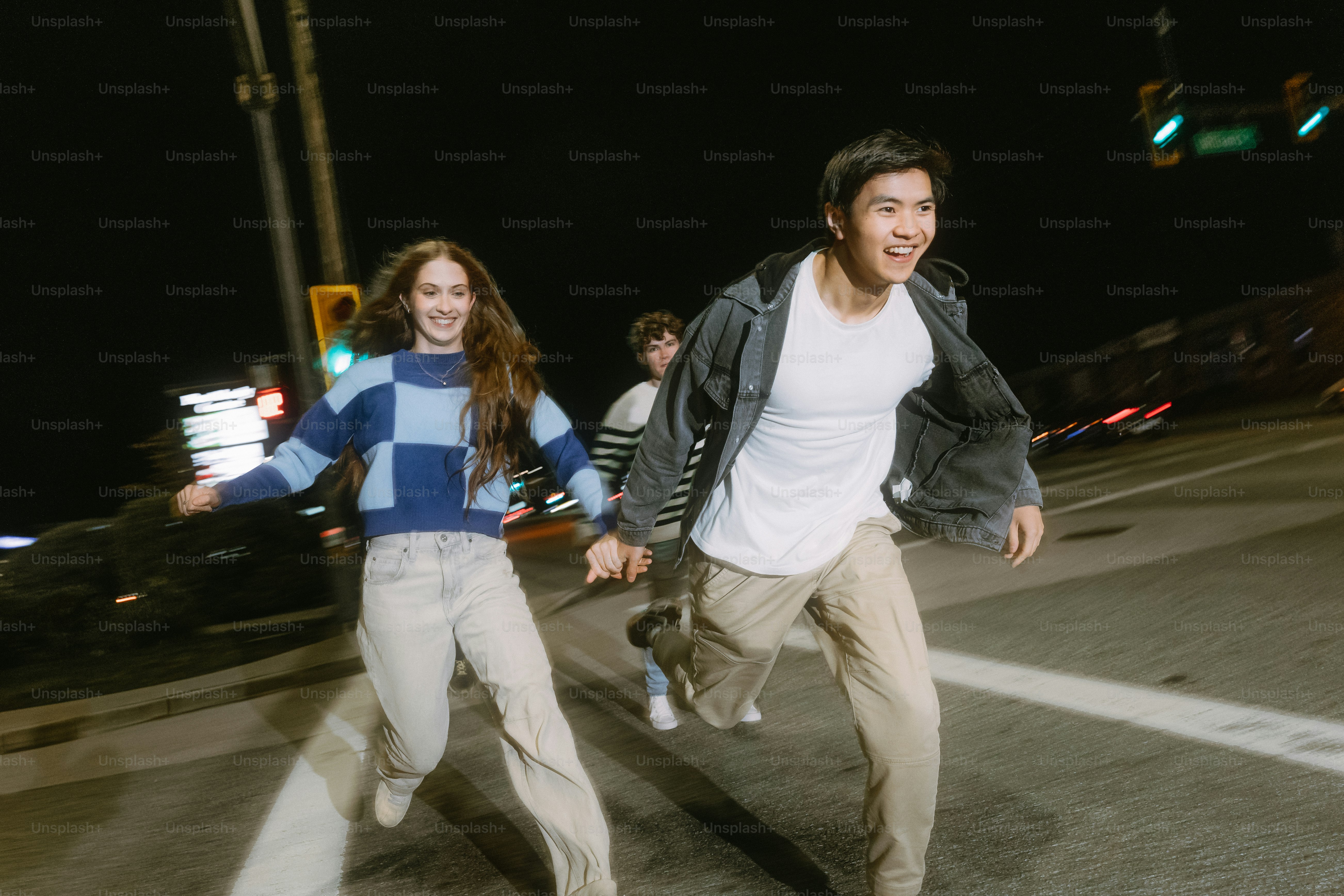 Three people running across a city street at night with motion blur
