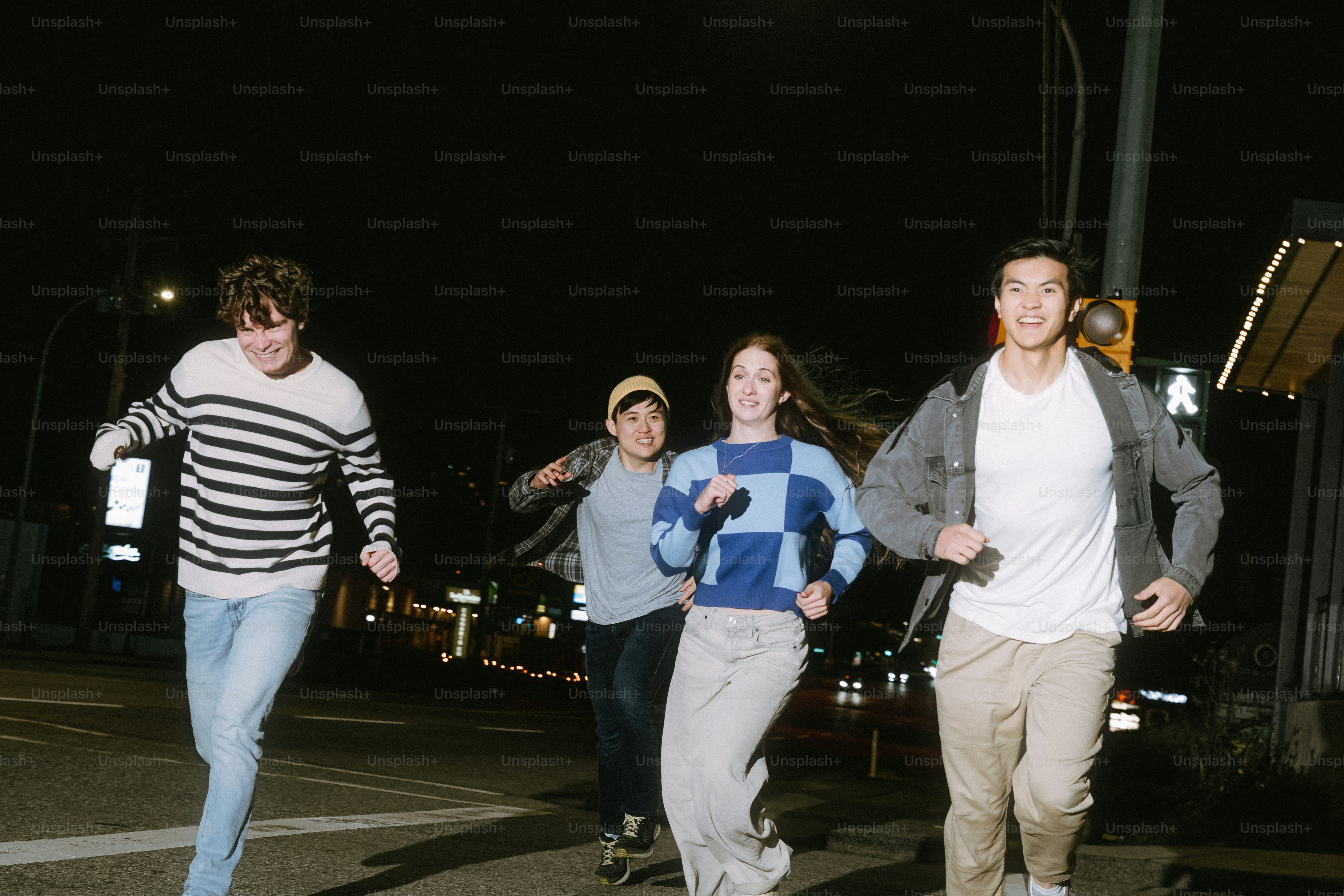 Four young adults running across a city street at night under streetlights