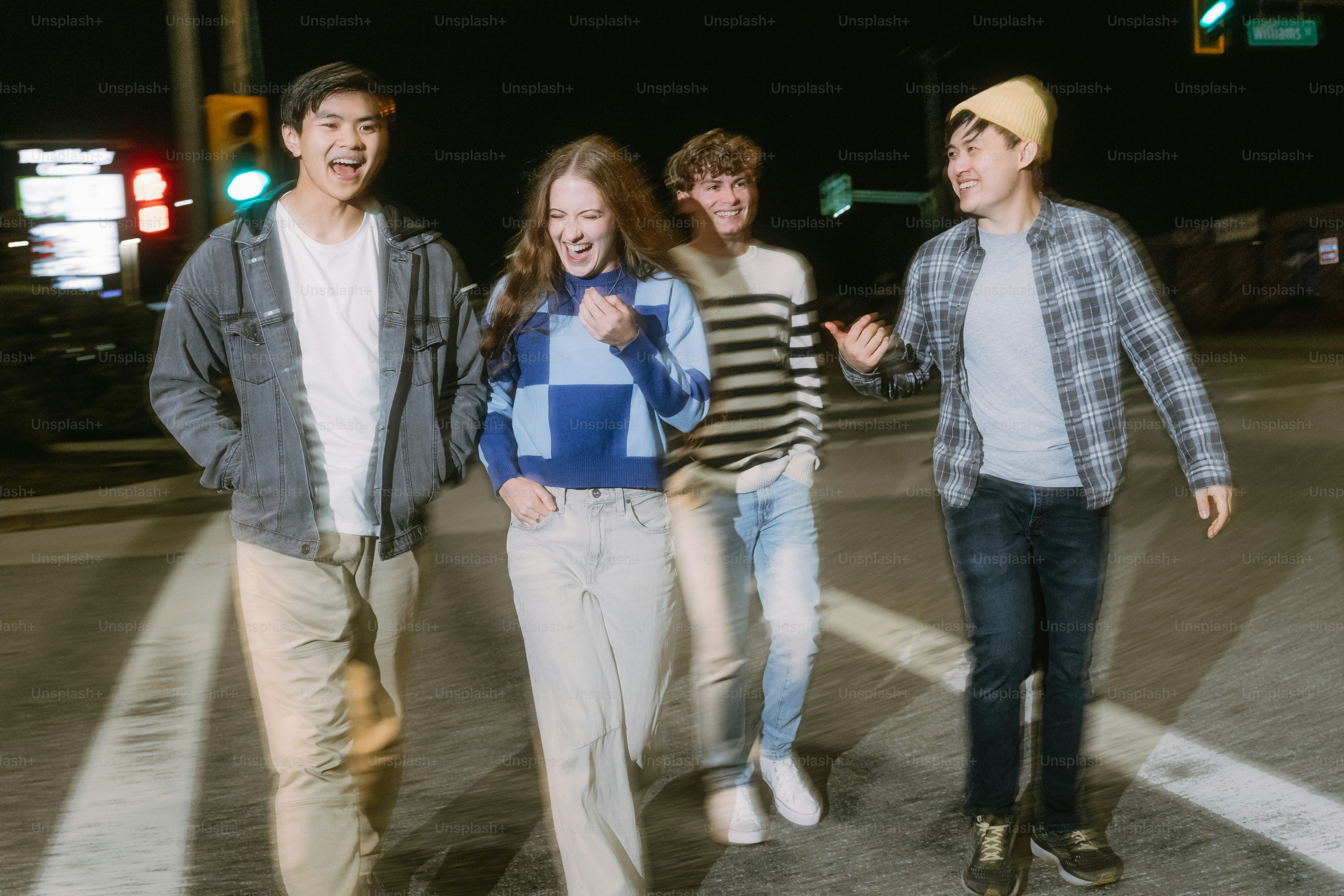 Four young adults laughing while walking across a city street at night