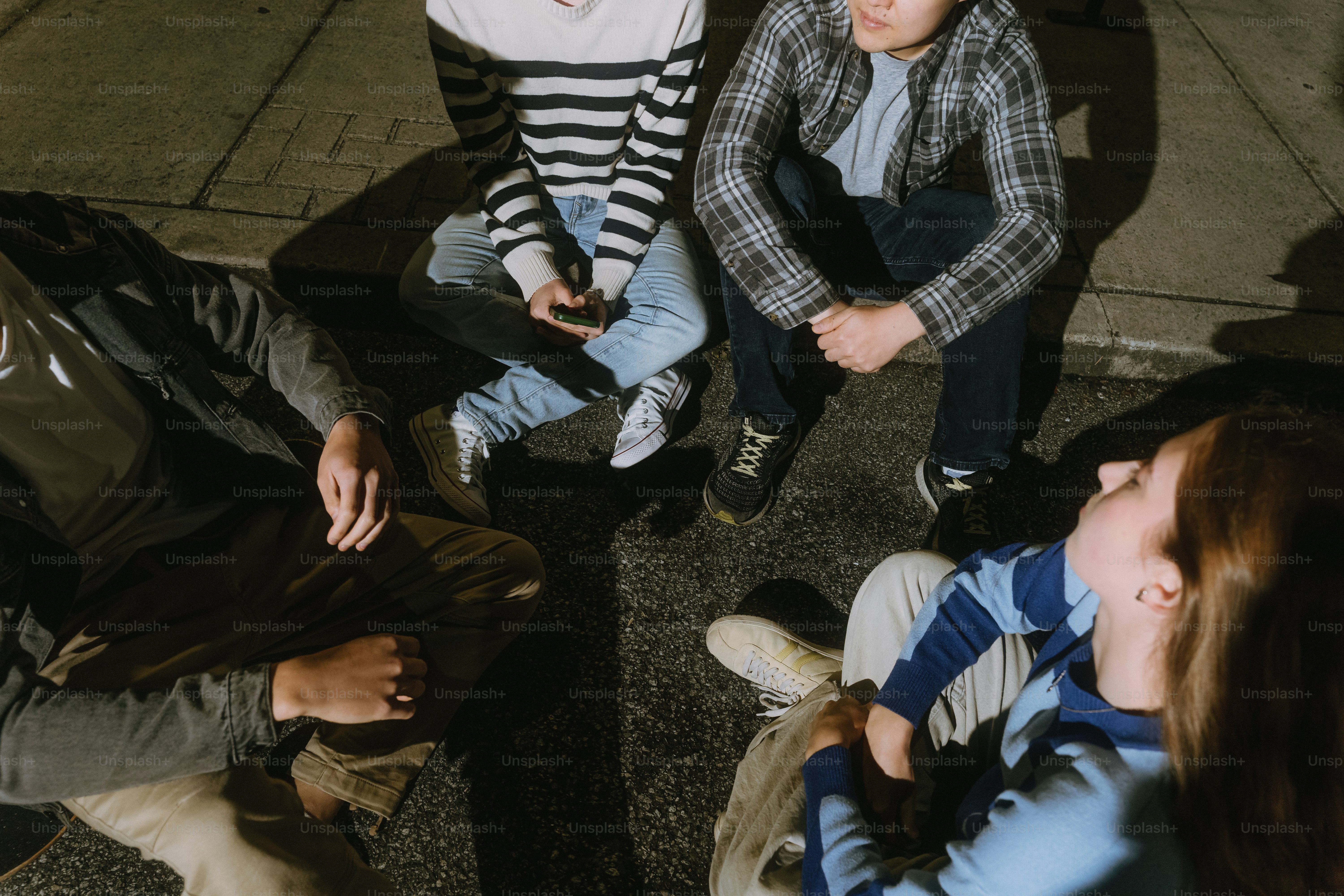 Four people sitting on a paved ground at night under bright overhead lighting
