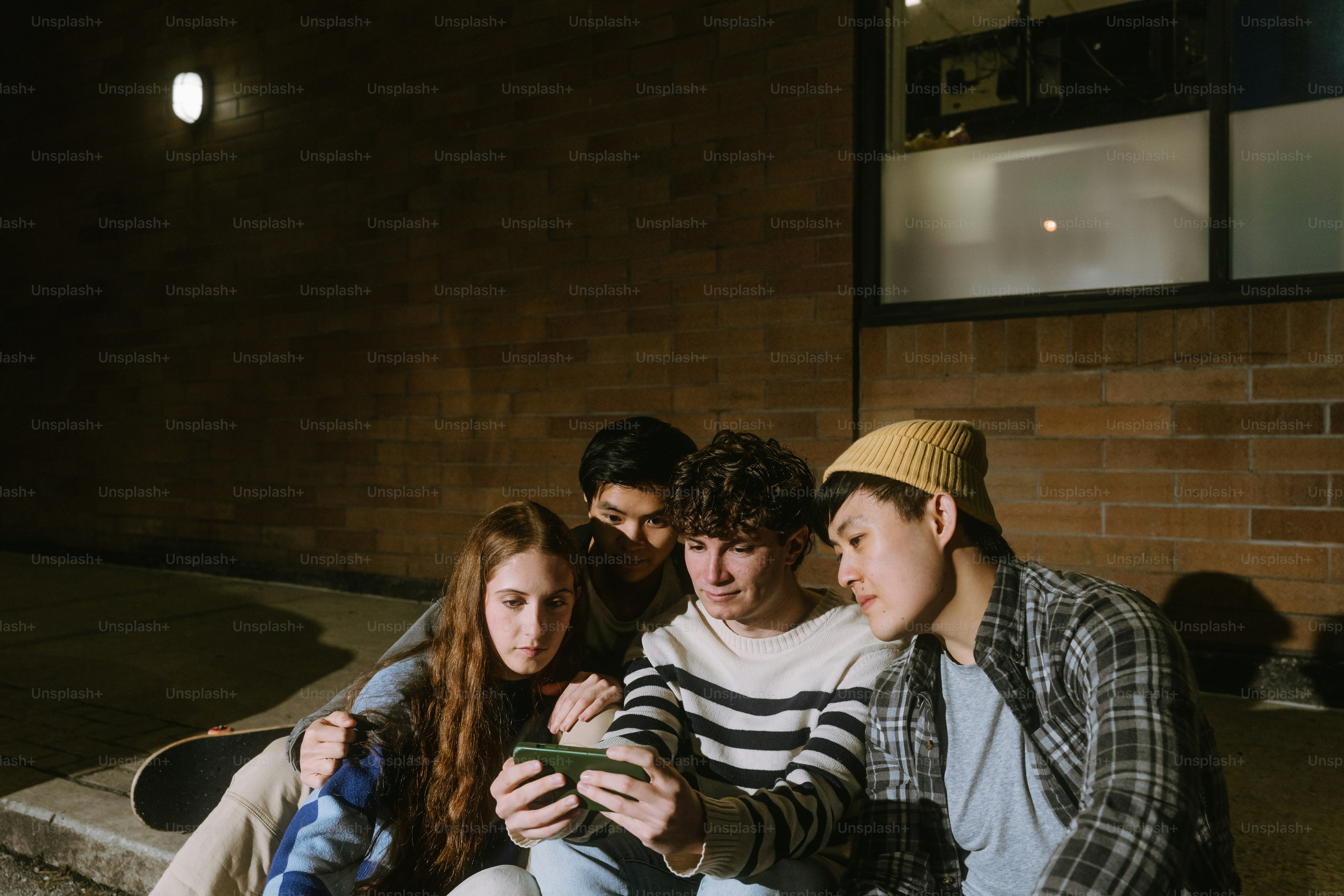 Four people sitting on a curb at night looking at a smartphone screen