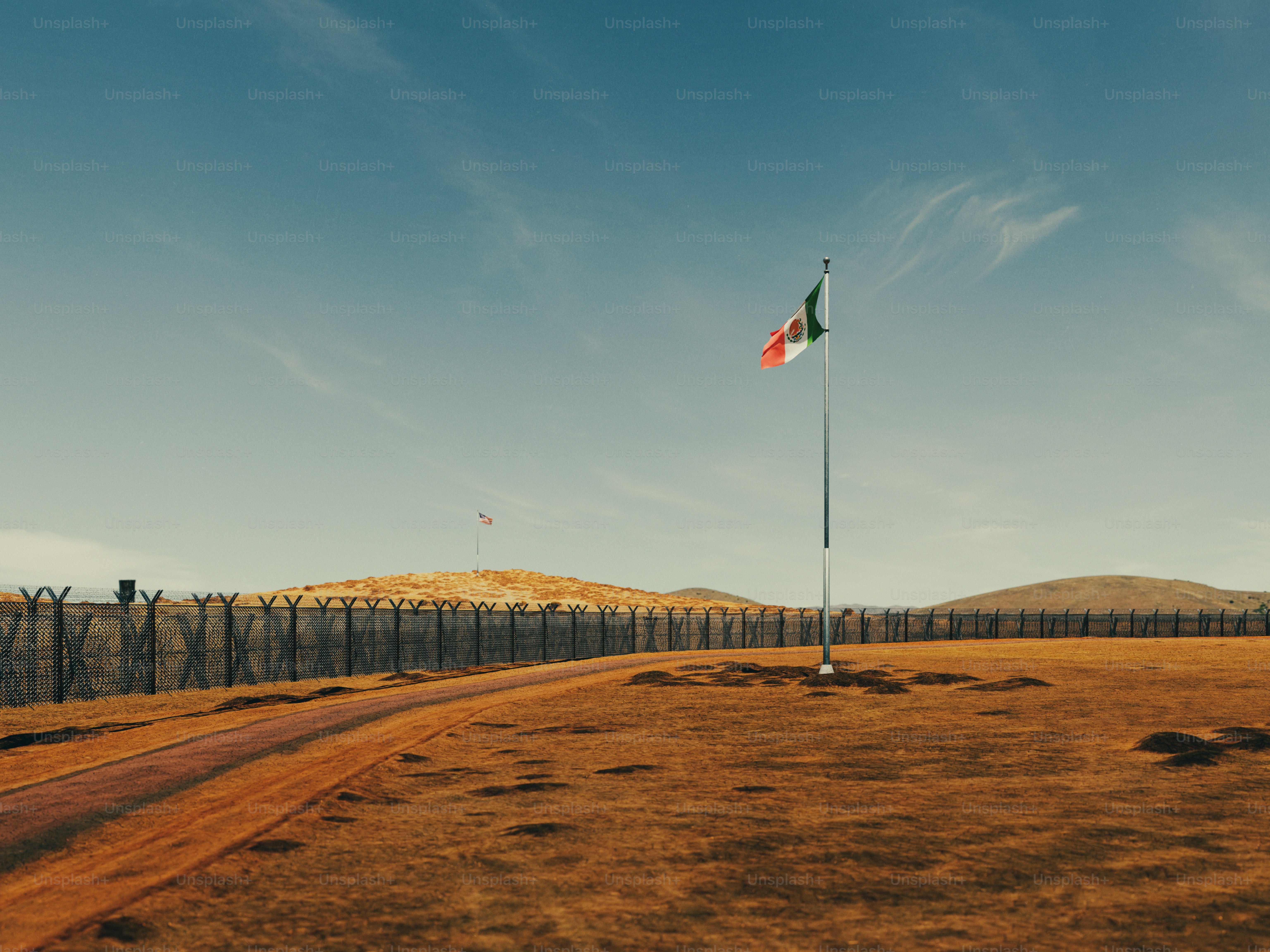 La bandera de México ondeando en un asta cerca de una valla fronteriza de alambre de espino
