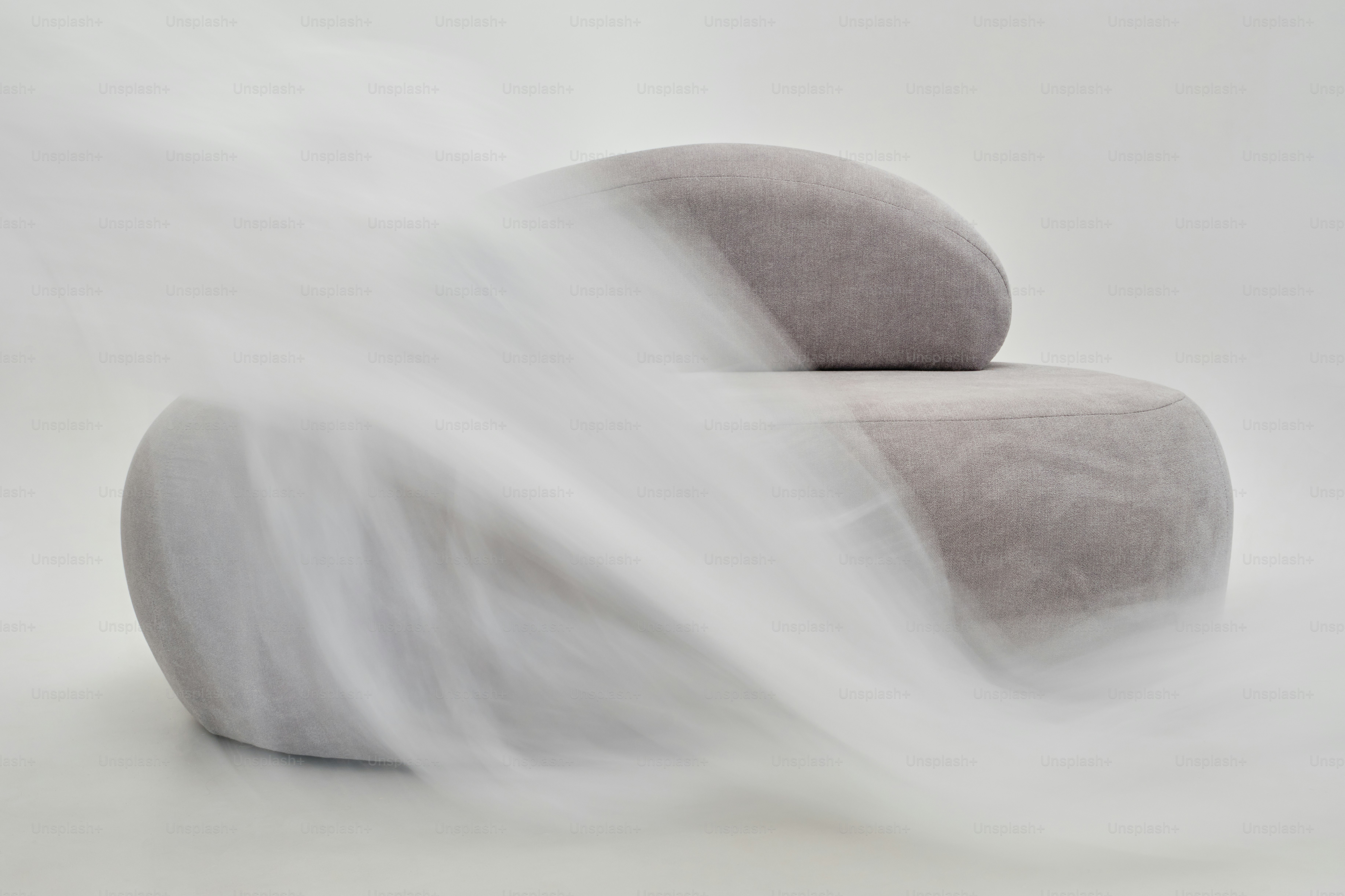 A modern grey upholstered armchair partially obscured by a flowing white fabric veil