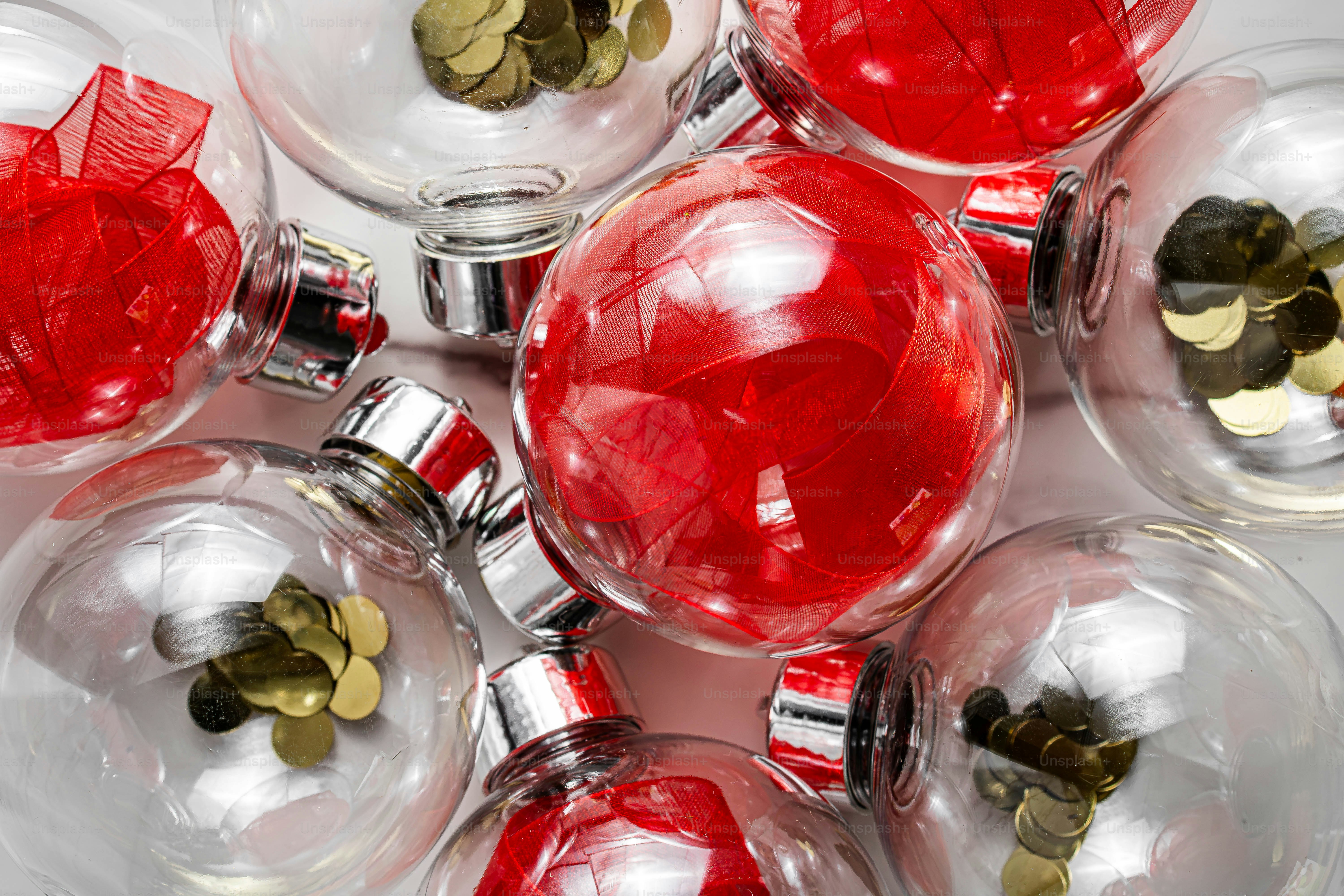 Adornos de cristal transparente rellenos con cinta roja o confeti dorado sobre una superficie blanca