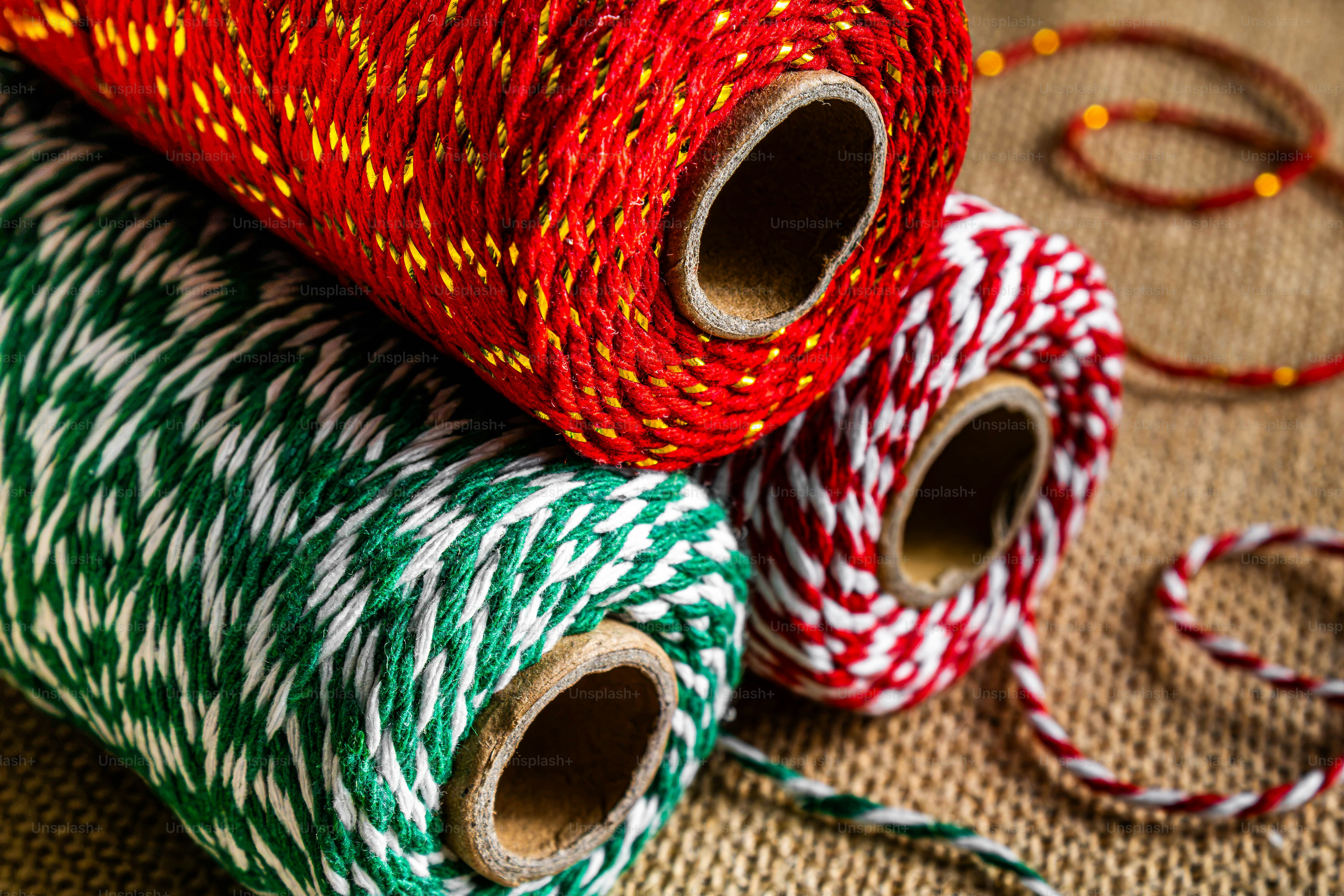 Tres carretes de cuerda festiva roja, verde y blanca de panadería sobre una superficie de arpillera