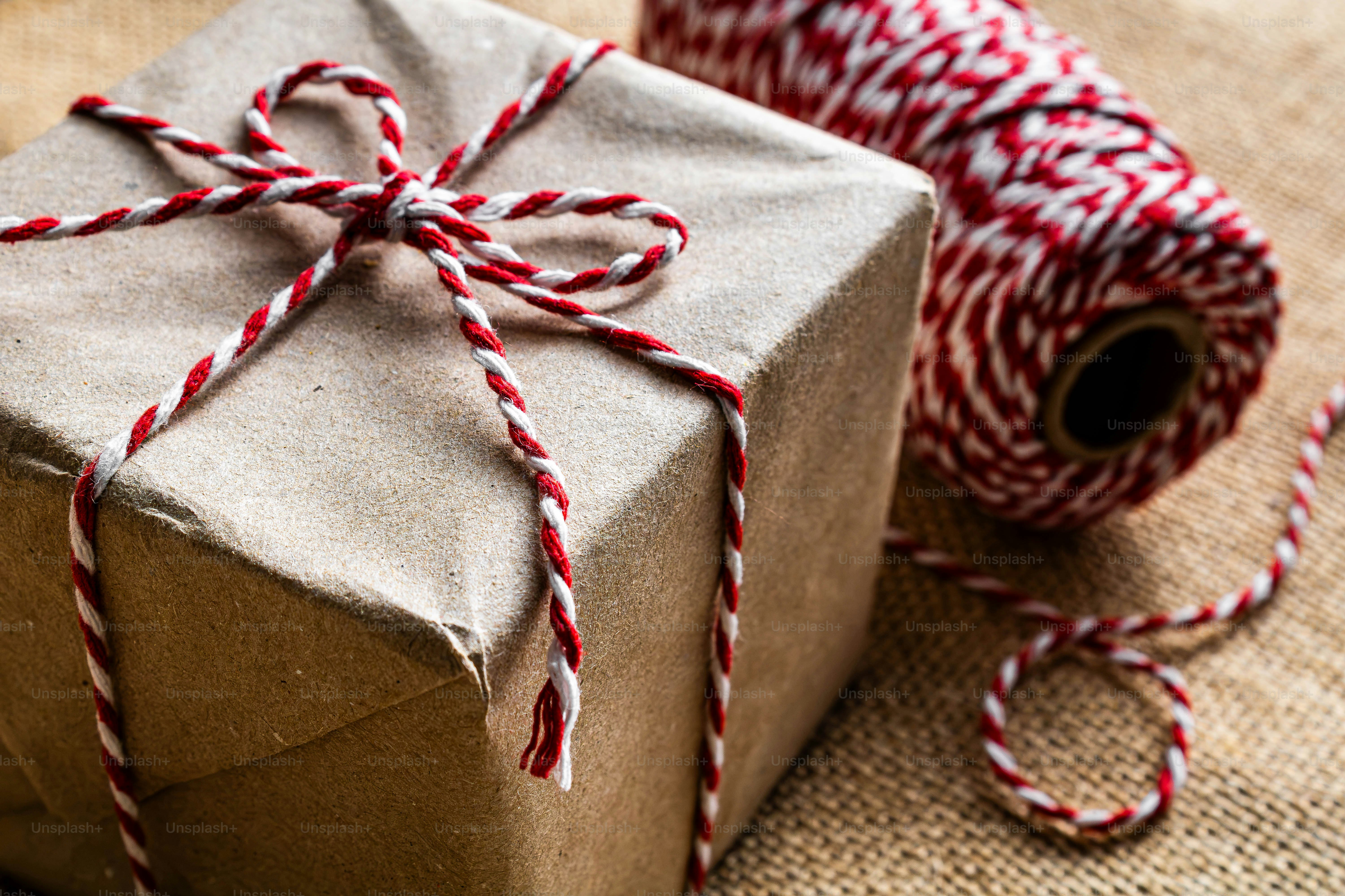 Una caja de regalo cuadrada envuelta en papel marrón atada con cuerda roja y blanca