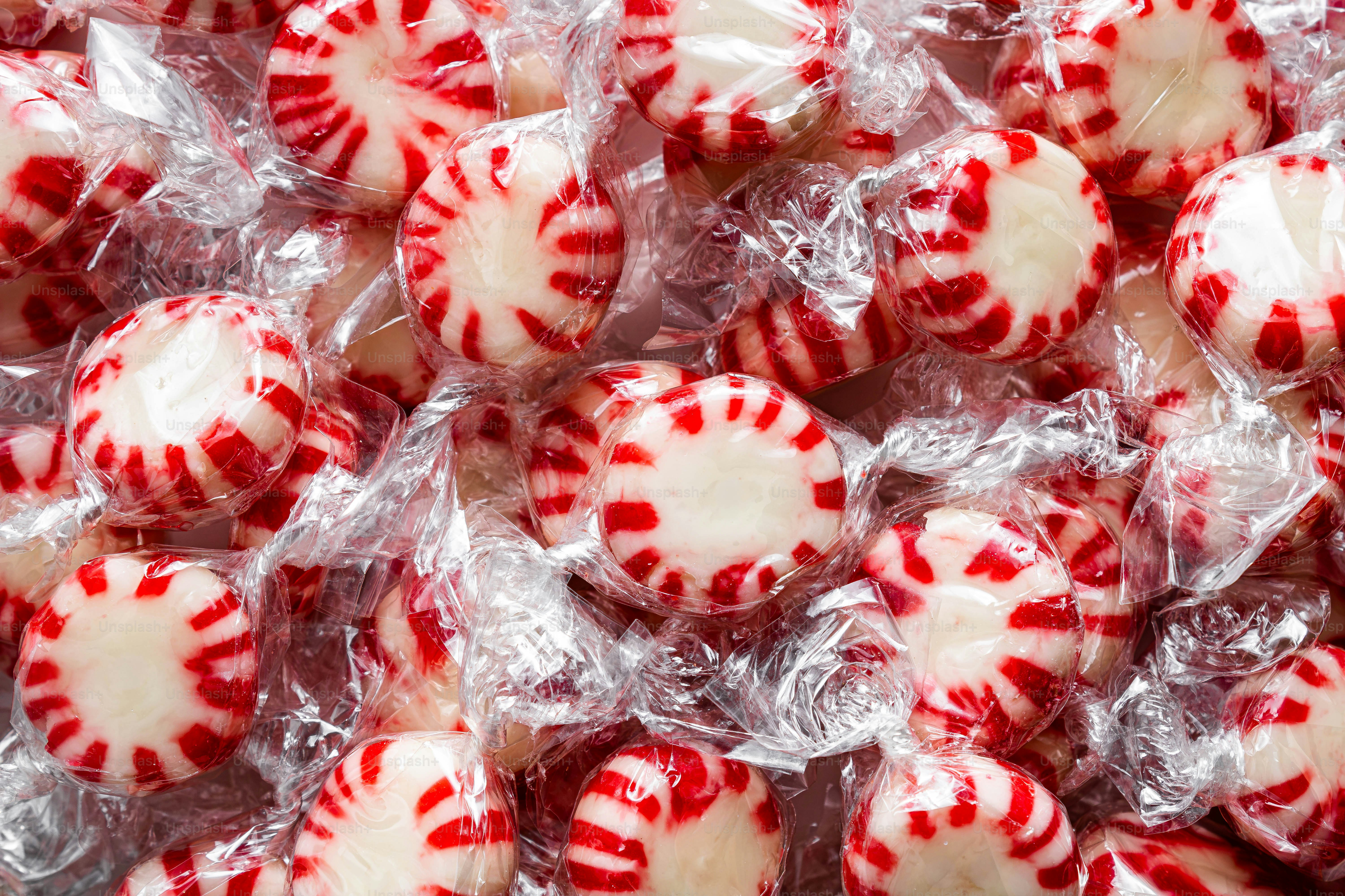 Un montón de caramelos redondos de menta con rayas rojas y blancas en envoltorios de plástico transparente