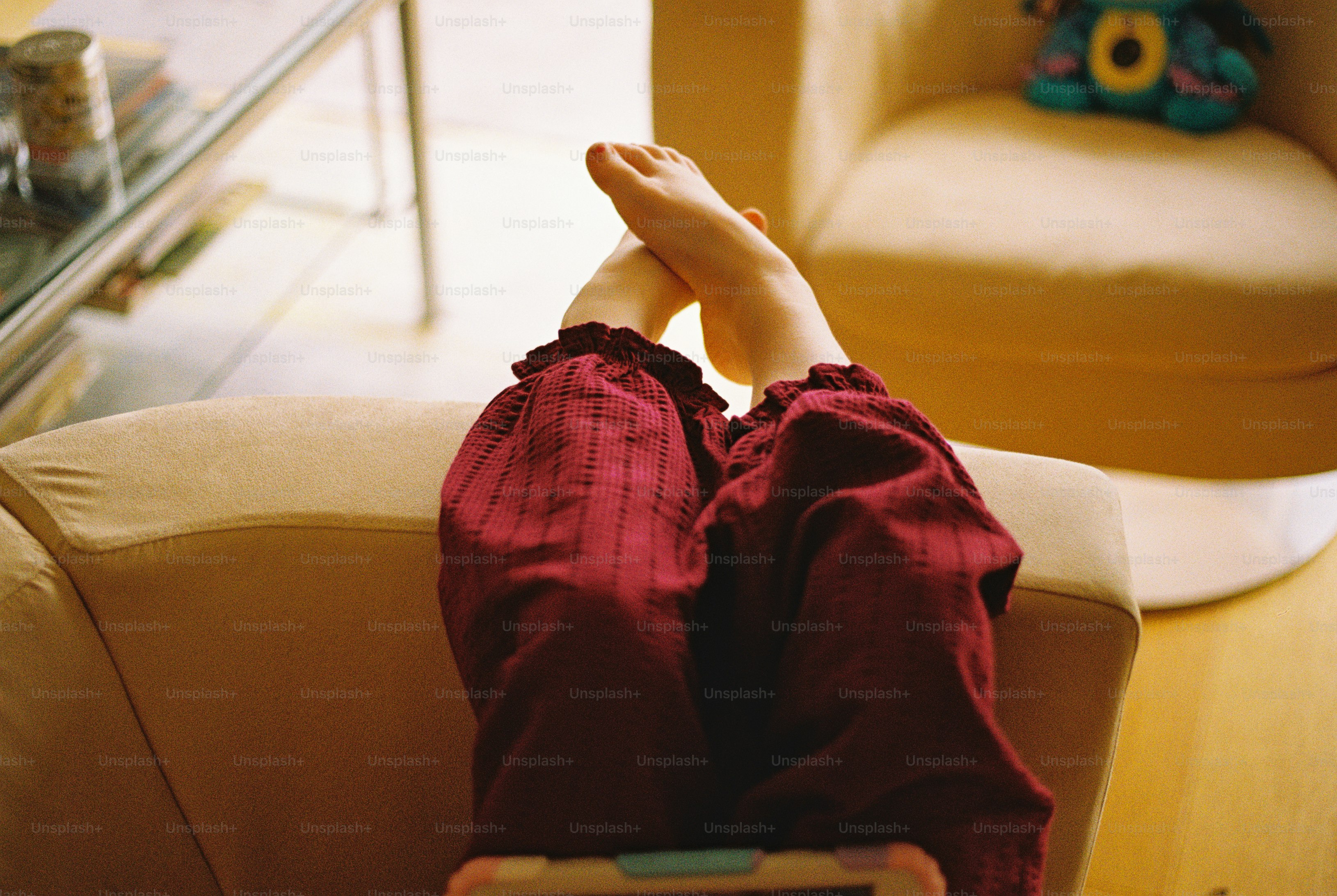 Bare feet and maroon textured trousers resting on the arm of a beige armchair